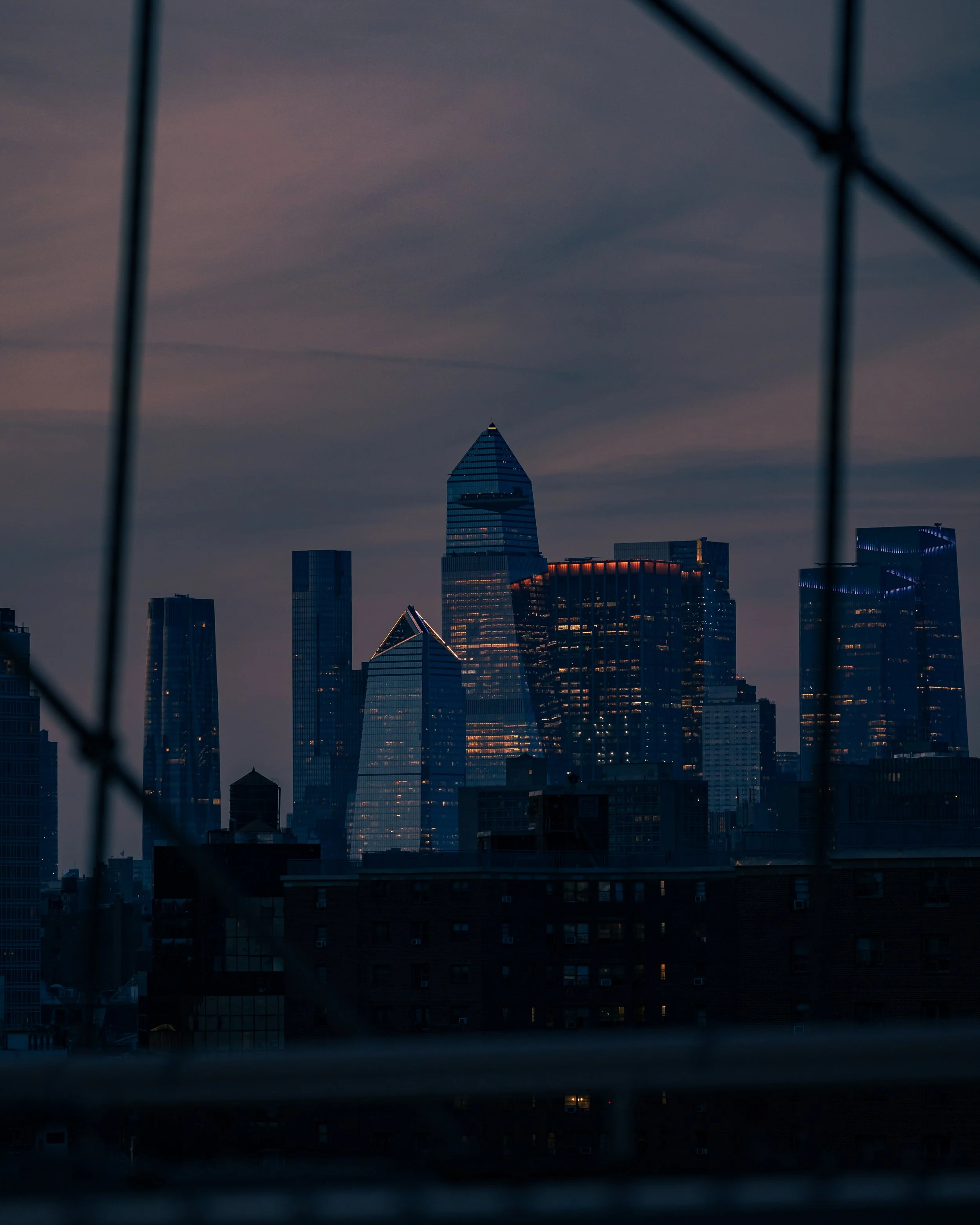 City skyline at dusk with modern skyscrapers viewed through a window with metal bars.