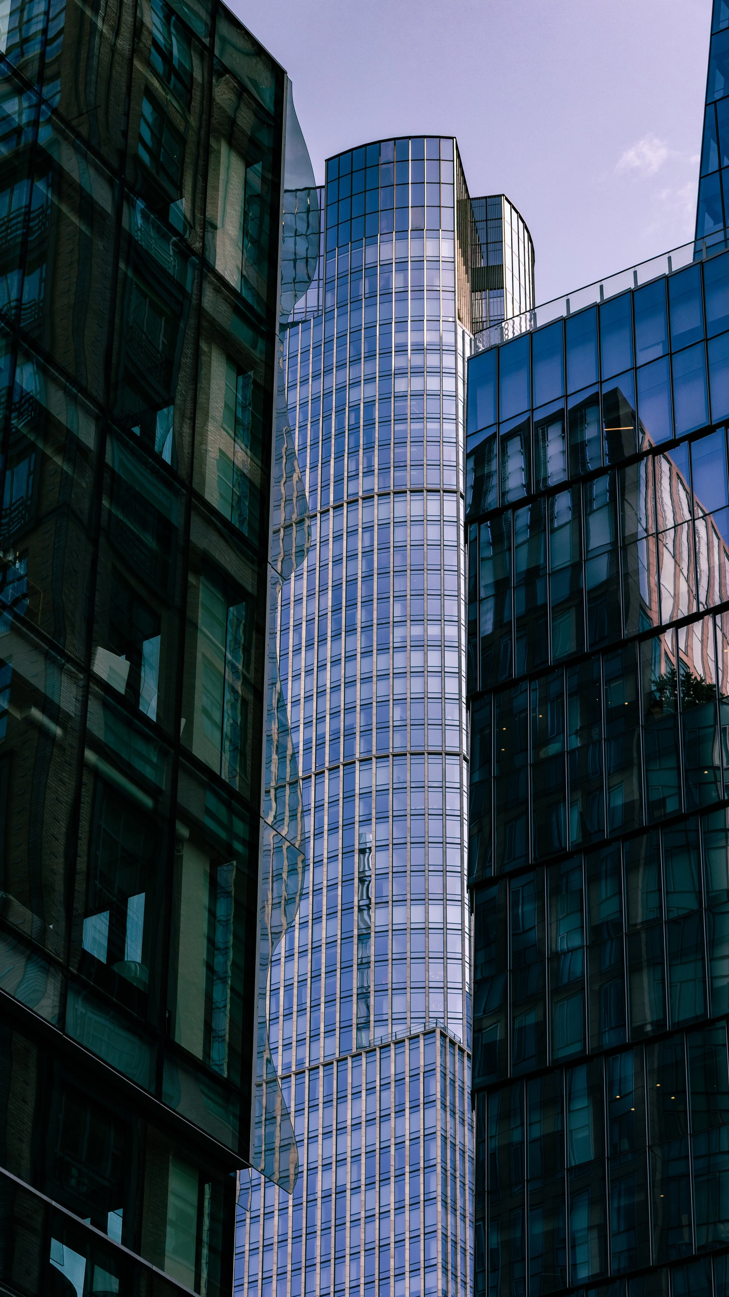 Looking up at modern glass skyscrapers with a partly cloudy sky in the background.