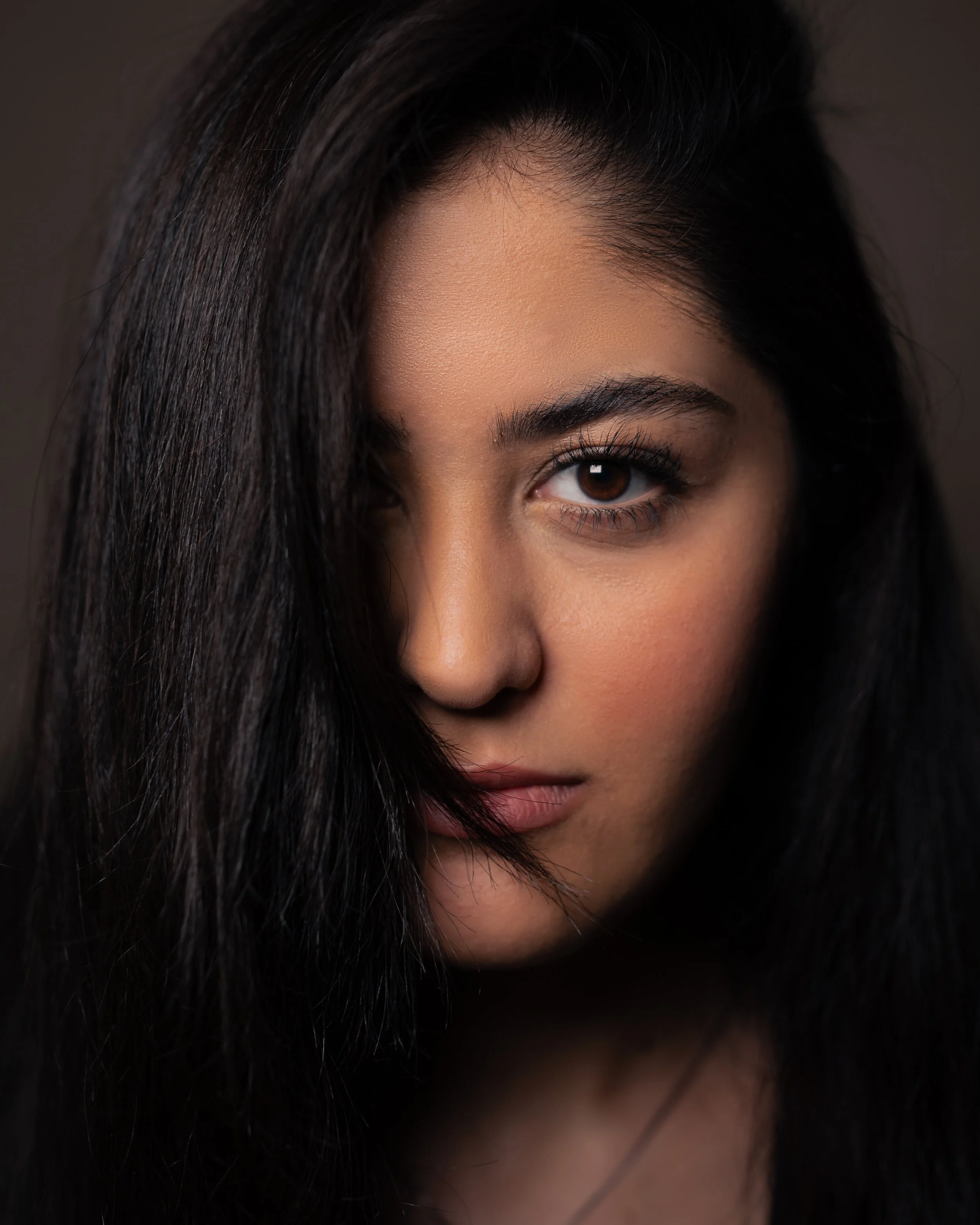 Close-up of a woman's face showing her eye, eyebrow, and dark hair partially covering her face.