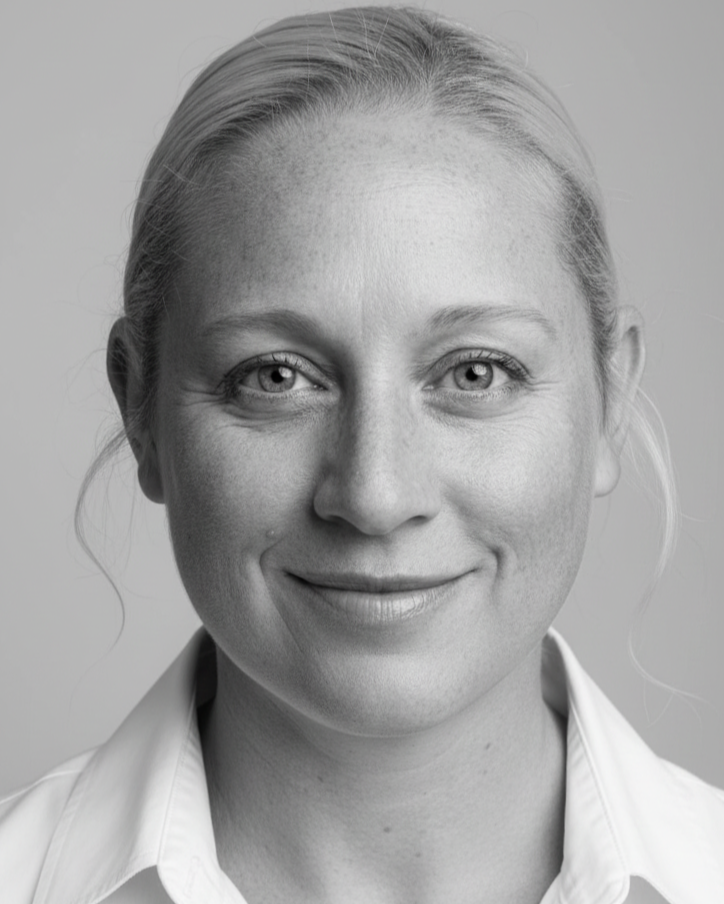 Close-up black-and-white portrait of a smiling woman with light-colored eyes, light hair pulled back, wearing a collared shirt.