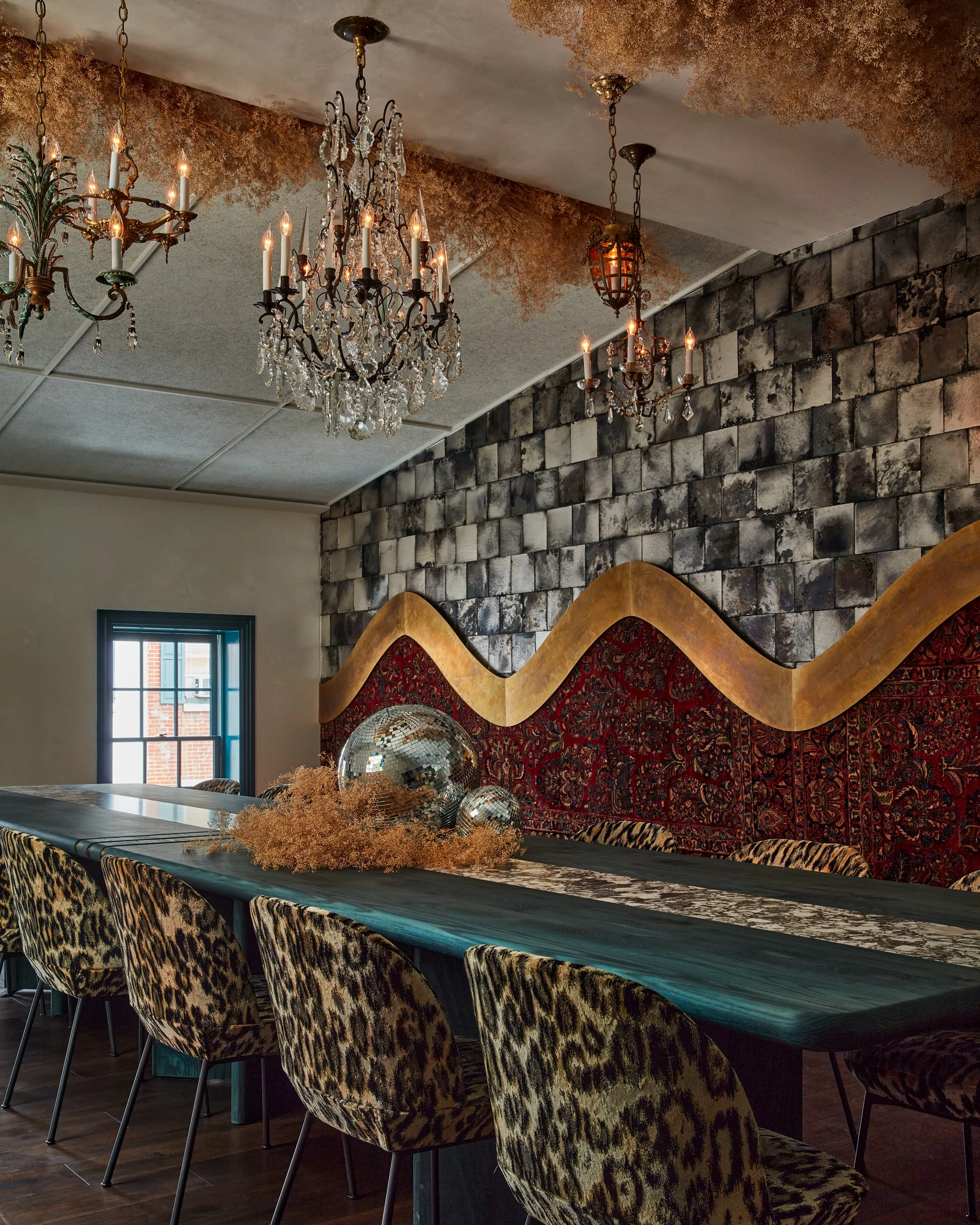 third floor private dining with custom table and finishes by velocette studio.  the wall has three finishes which include mirror mosaic patinated brass and red persian rug 