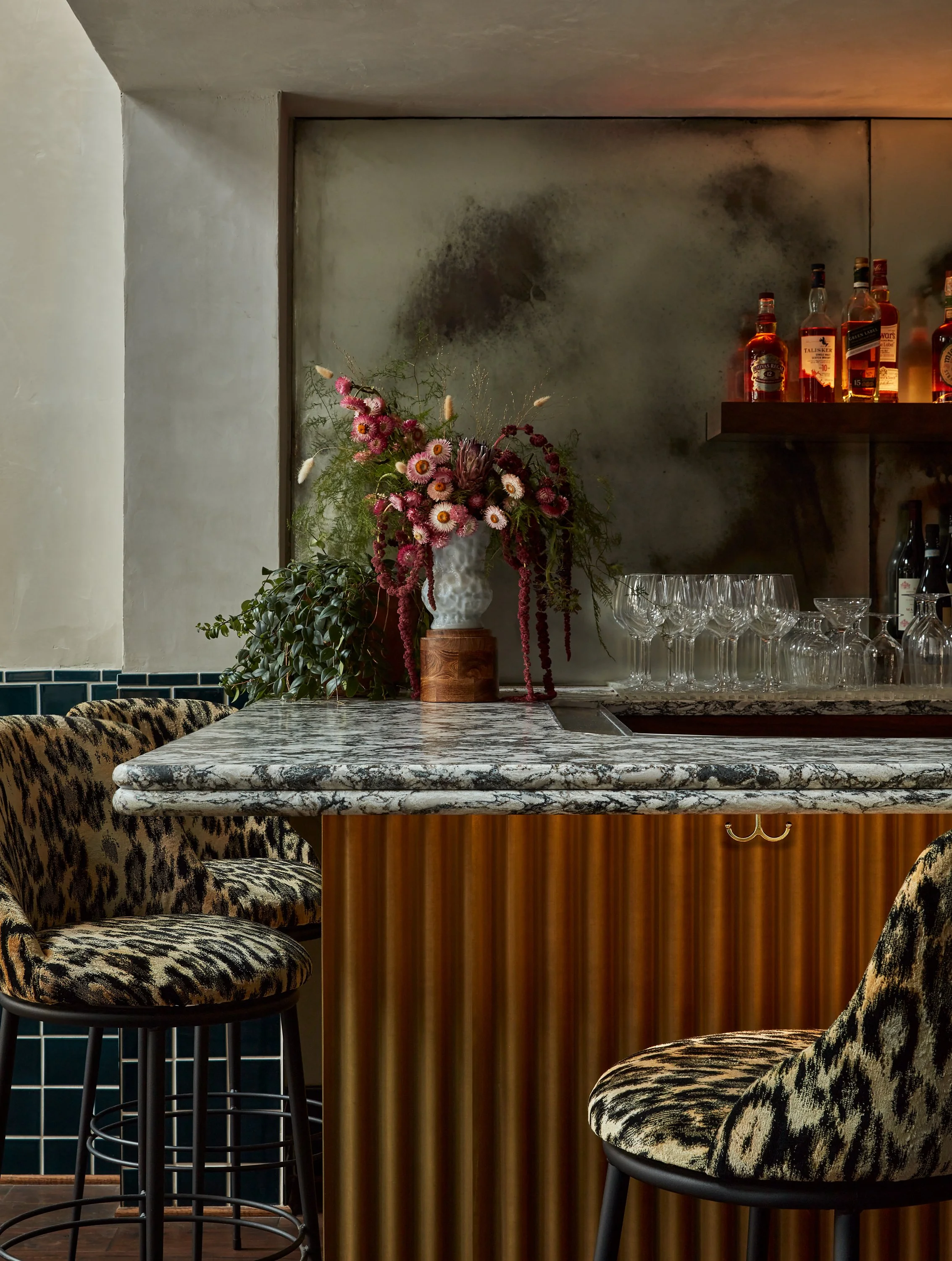 large scale leopard print bar stools in front of bar finished in brass and topped with stone
