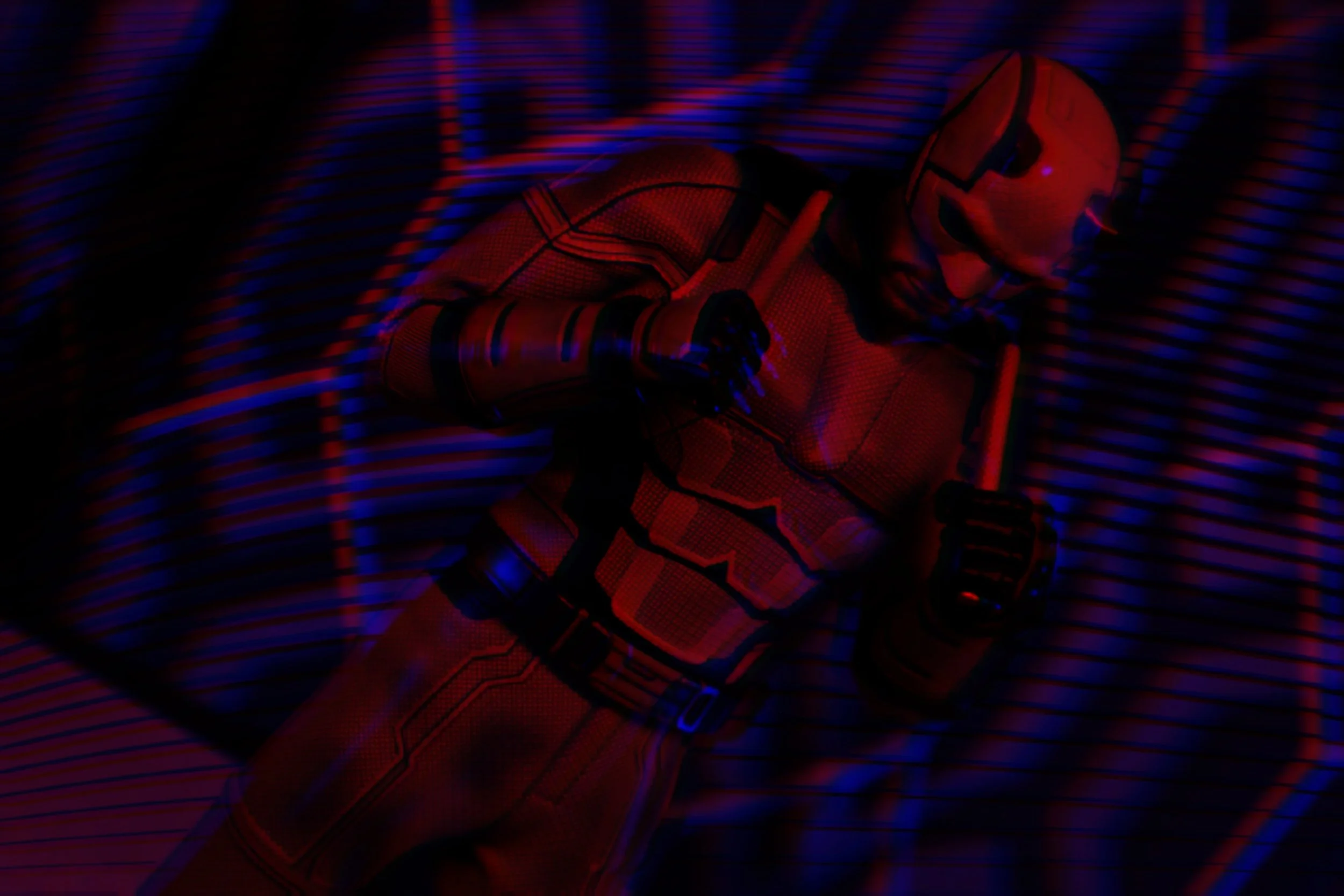 A person dressed as Spider-Man in a dark environment with red and blue led lights, lying down with hands in front of them.