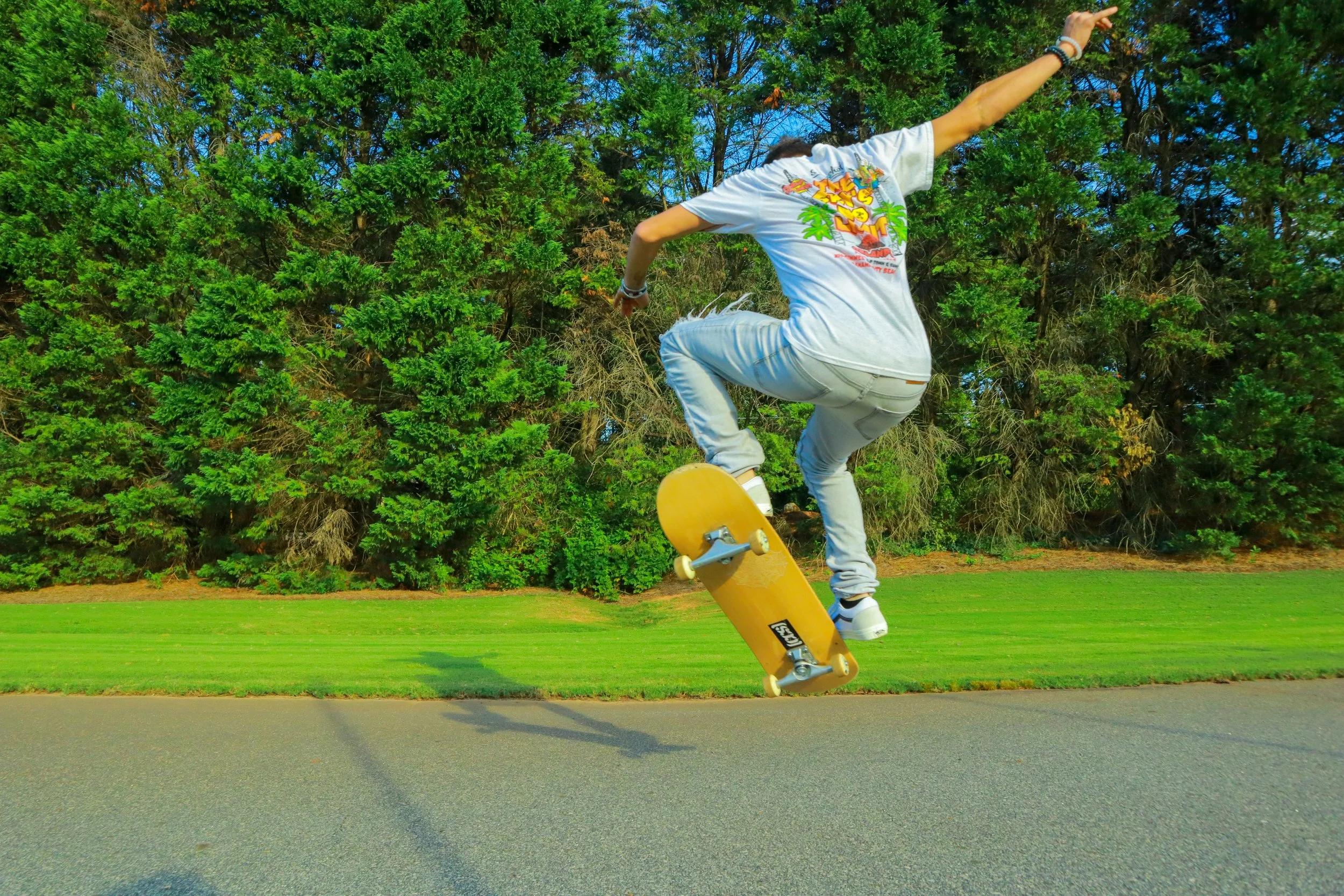 A person performing a skateboard trick in a park with green grass and tall trees in the background.