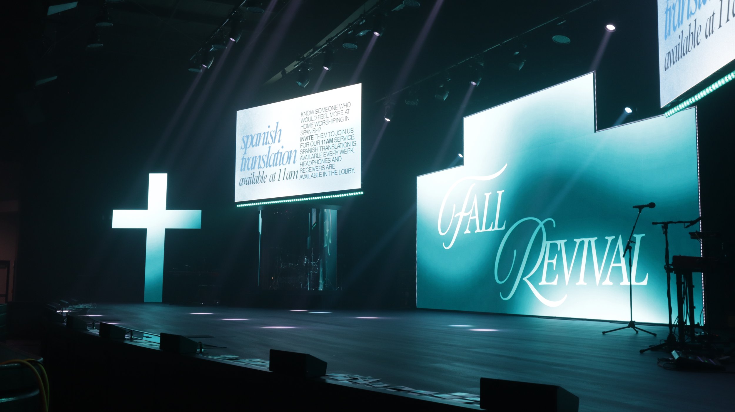 Stage with large screens displaying text about Spanish translation services, microphones, and a cross symbol.