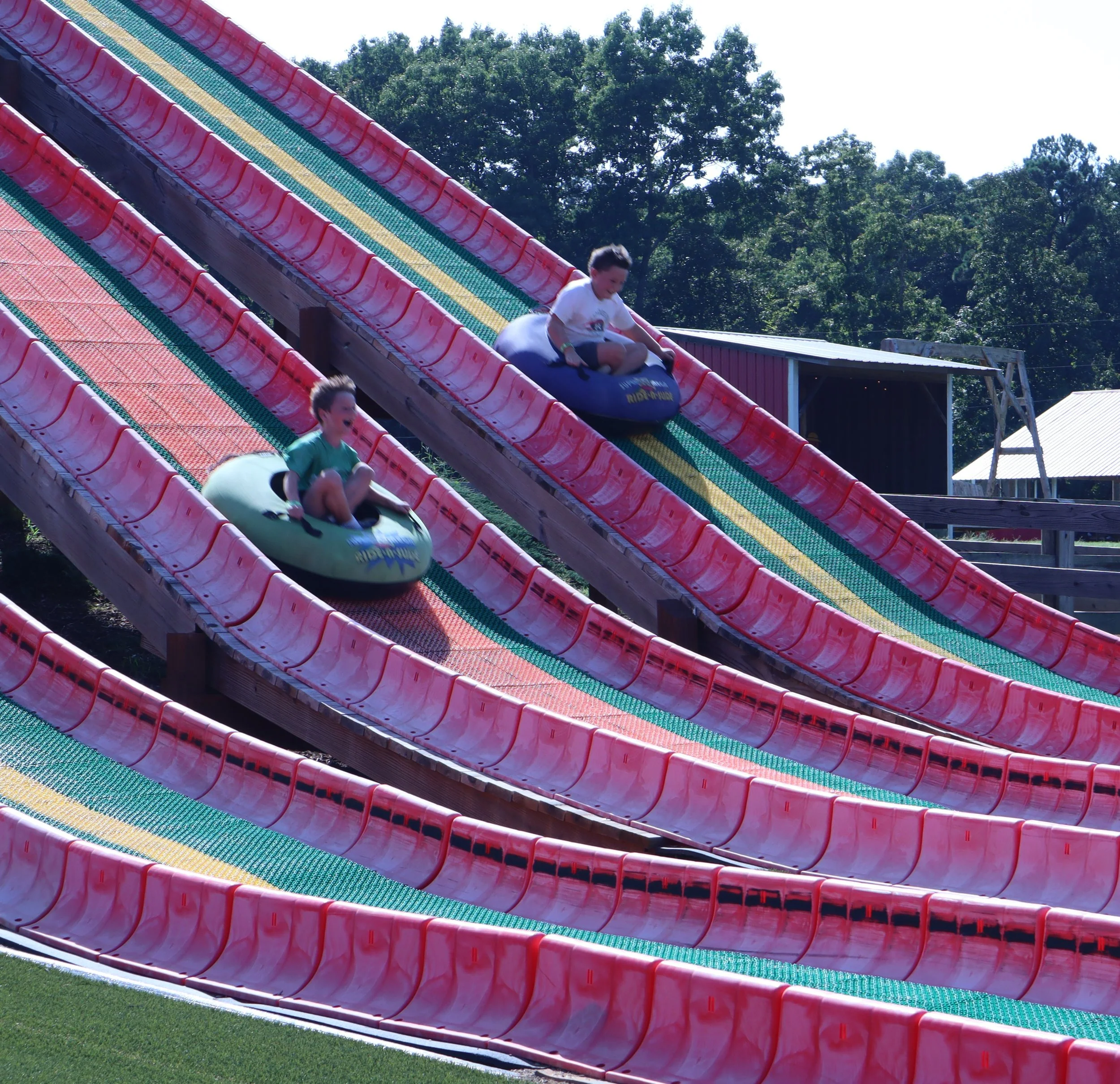 Children riding down a large colorful water slide outdoors surrounded by trees.