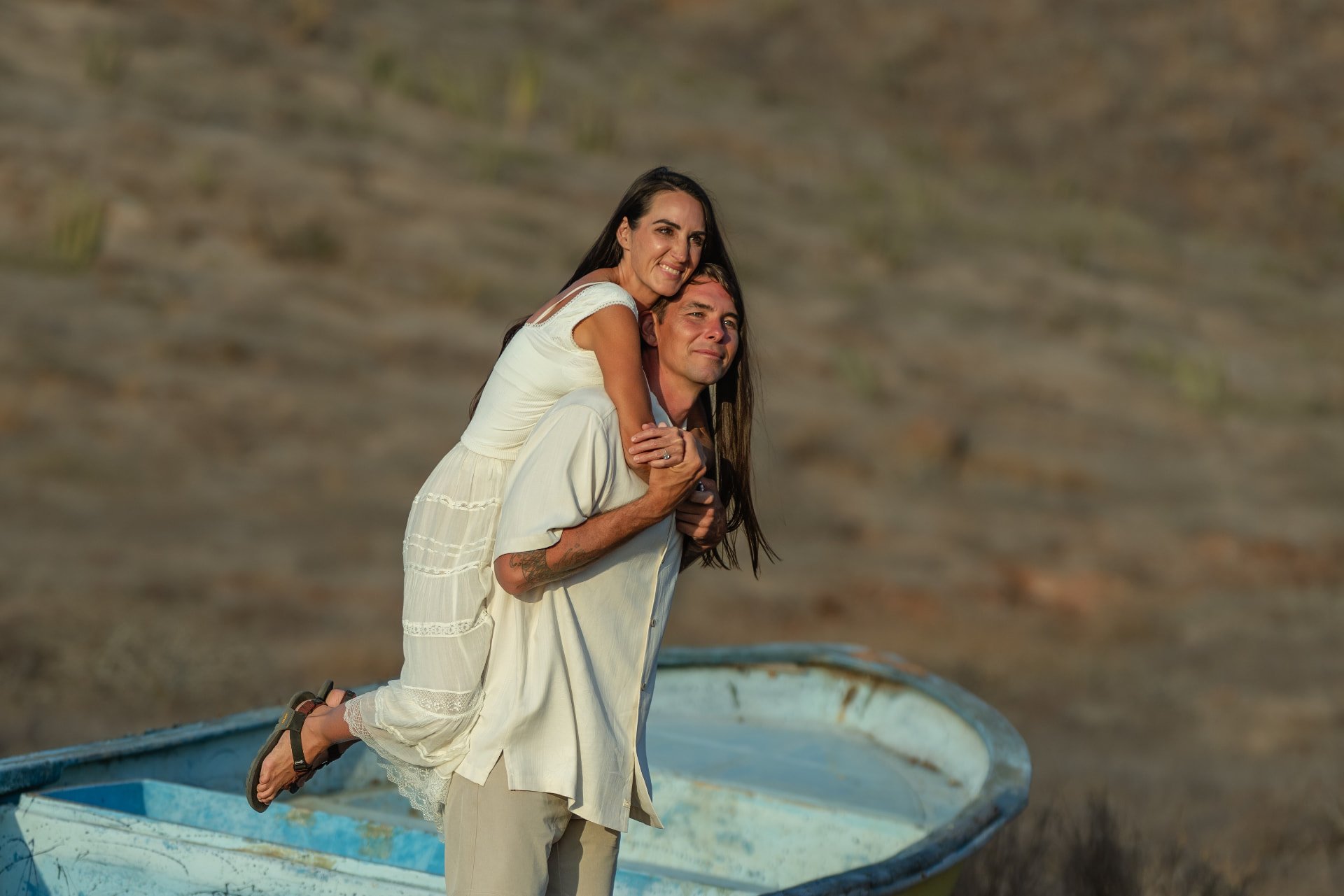 A man giving a woman a piggyback ride on a boat with a rocky landscape in the background.