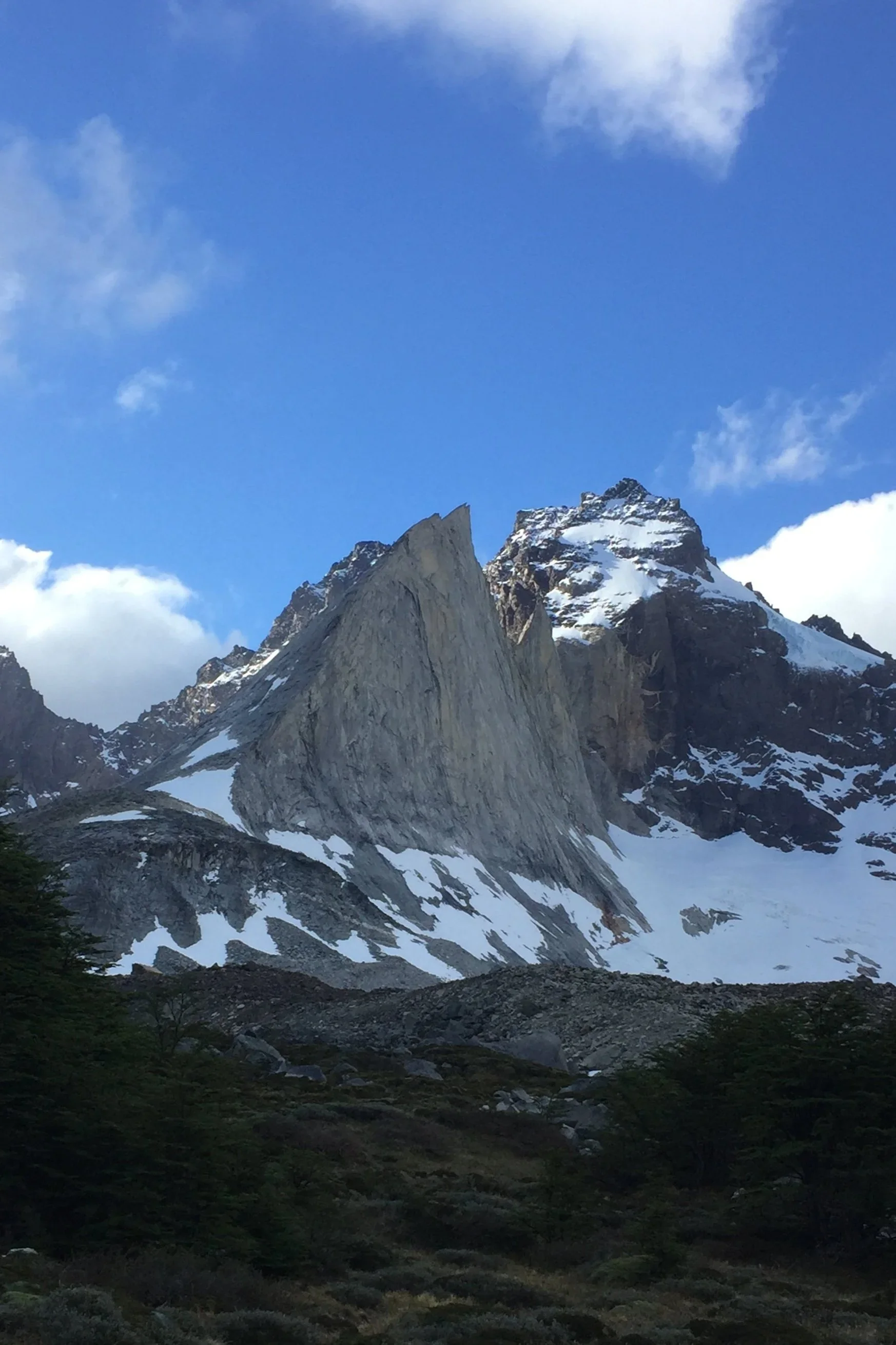 Mountain peaks with snow and rugged rocky terrain under a blue sky with scattered clouds.