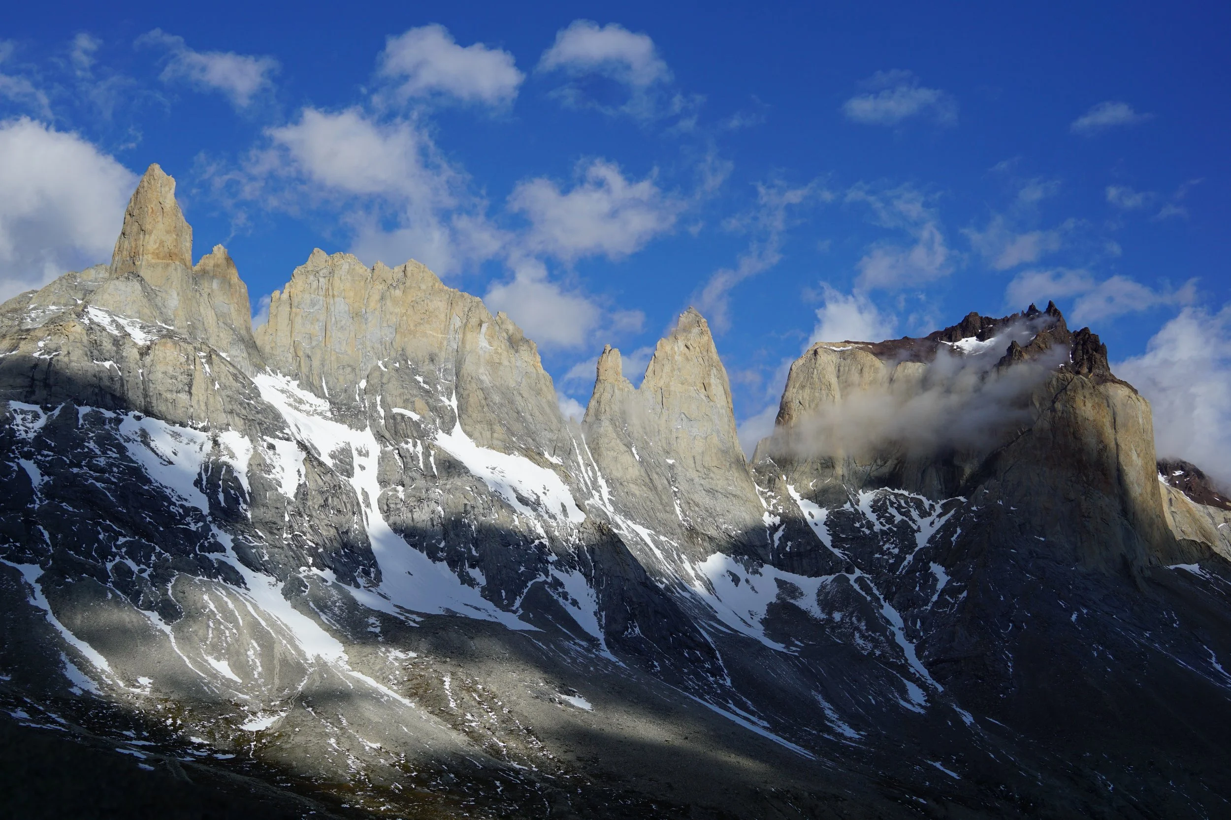Snow-capped mountain peaks with rugged rocky surfaces under a partly cloudy blue sky.
