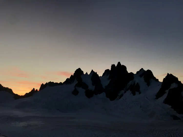 Snow-covered mountain range silhouette at sunset or sunrise with a gradient sky