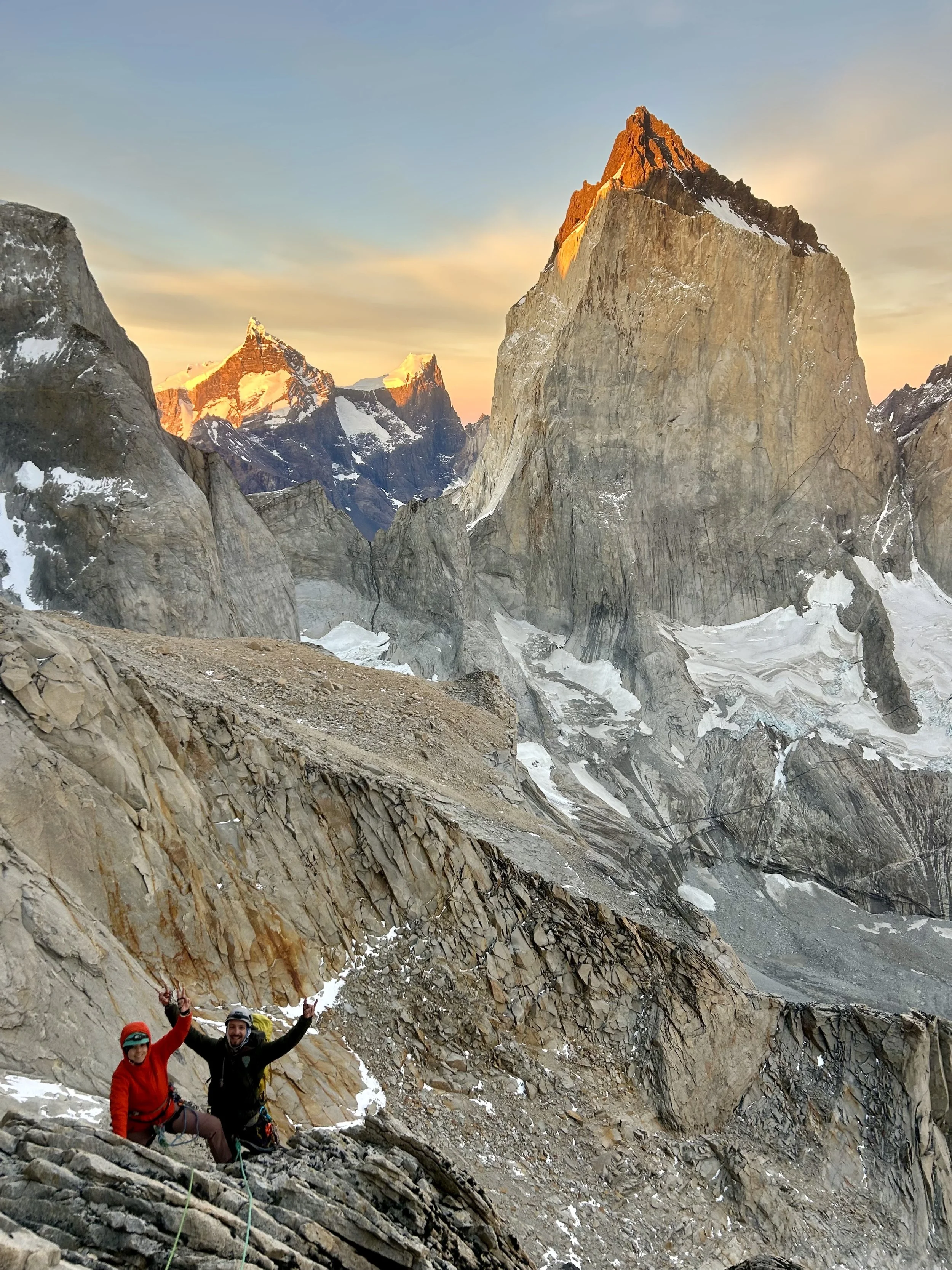 Two climbers on the North Tower of Paine, with a view of the Fortaleza and Escudo in the background at sunrise in Torres del Paine National Park. This is a multi pitch alpine rock climb in Torres del Paine