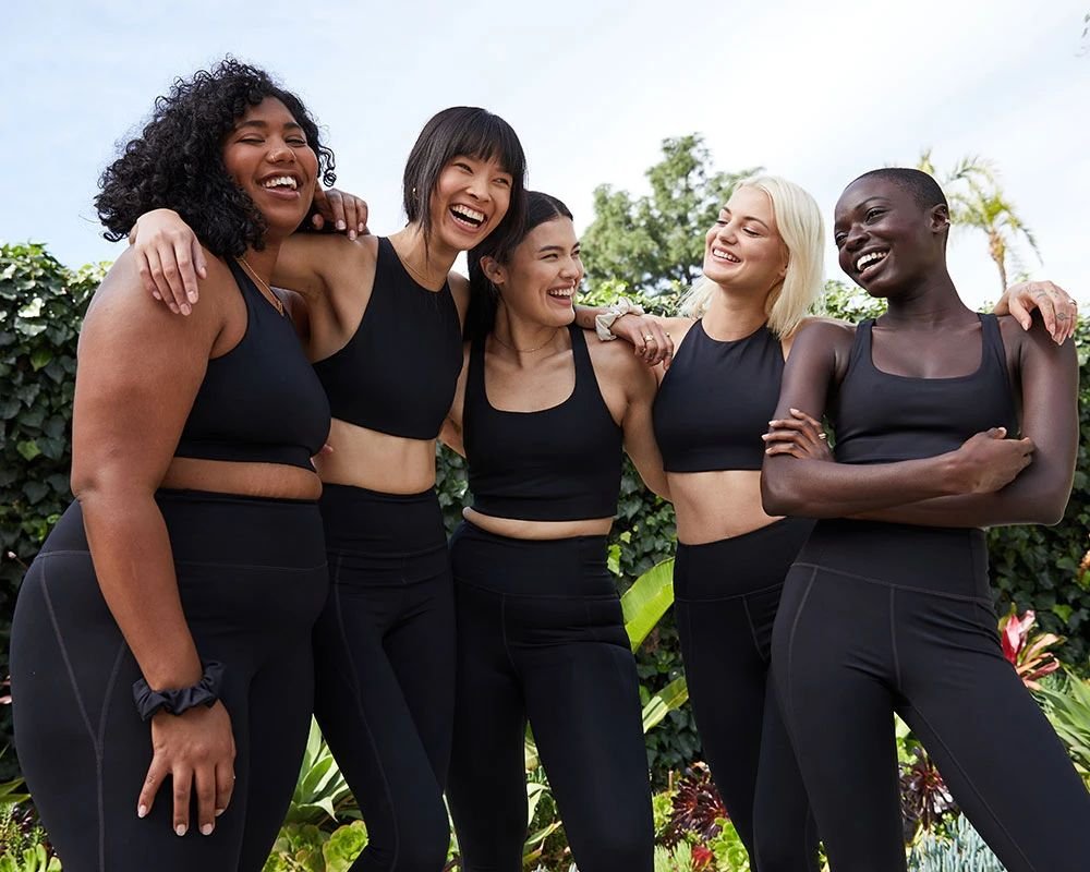 A group of five women in active wear, standing outside and smiling
