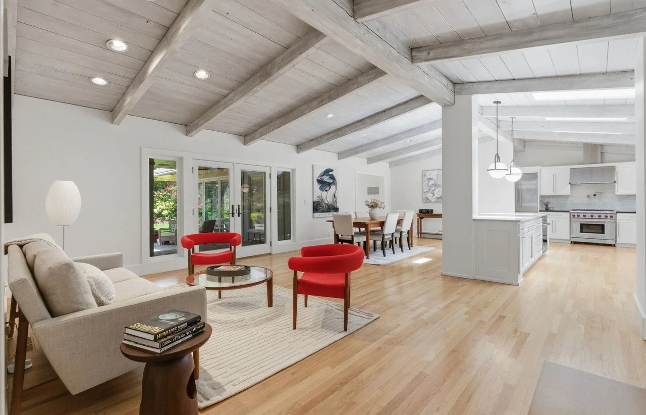 Great room with whitewashed beams, red accent chairs and an open kitchen