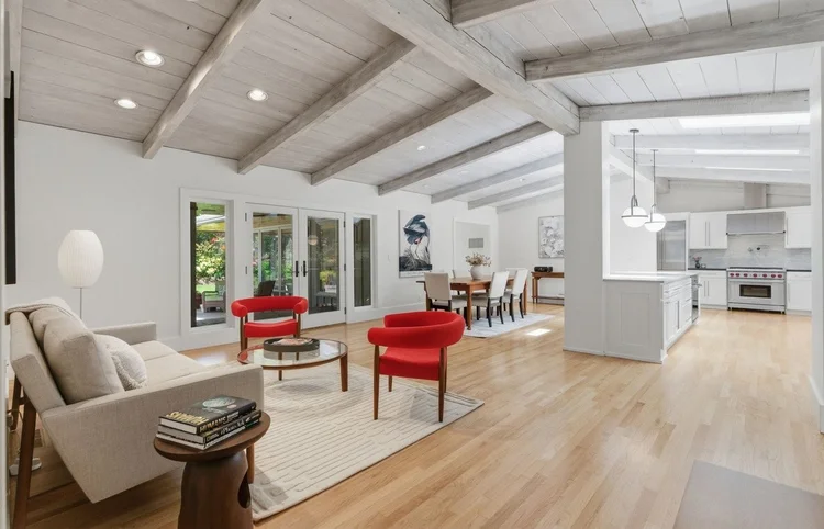 Great room with whitewashed beams, red accent chairs and an open kitchen