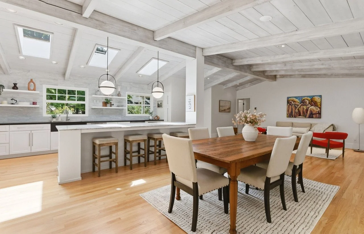 Dining table beside a long kitchen island under a beamed ceiling
