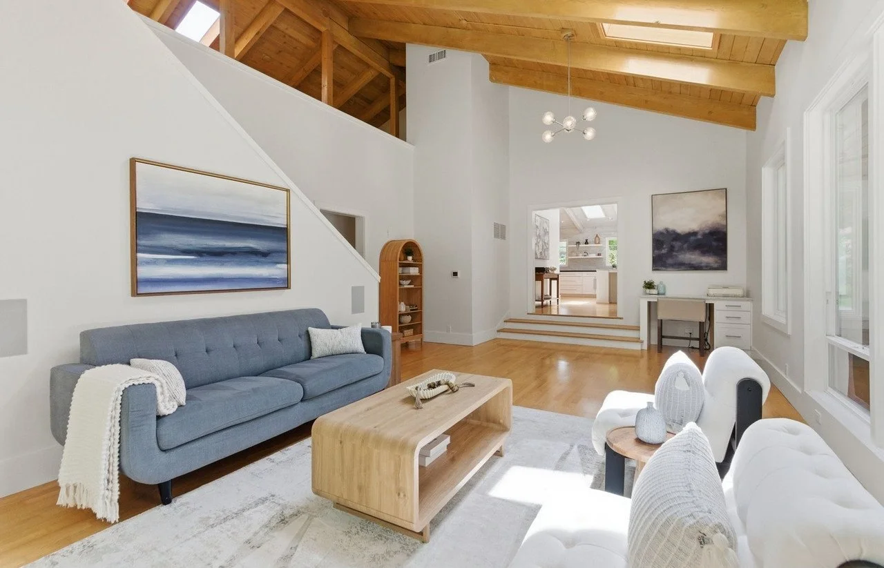 Living room with a blue tufted sofa, cream sofa and an arched bookcase under a beamed ceiling
