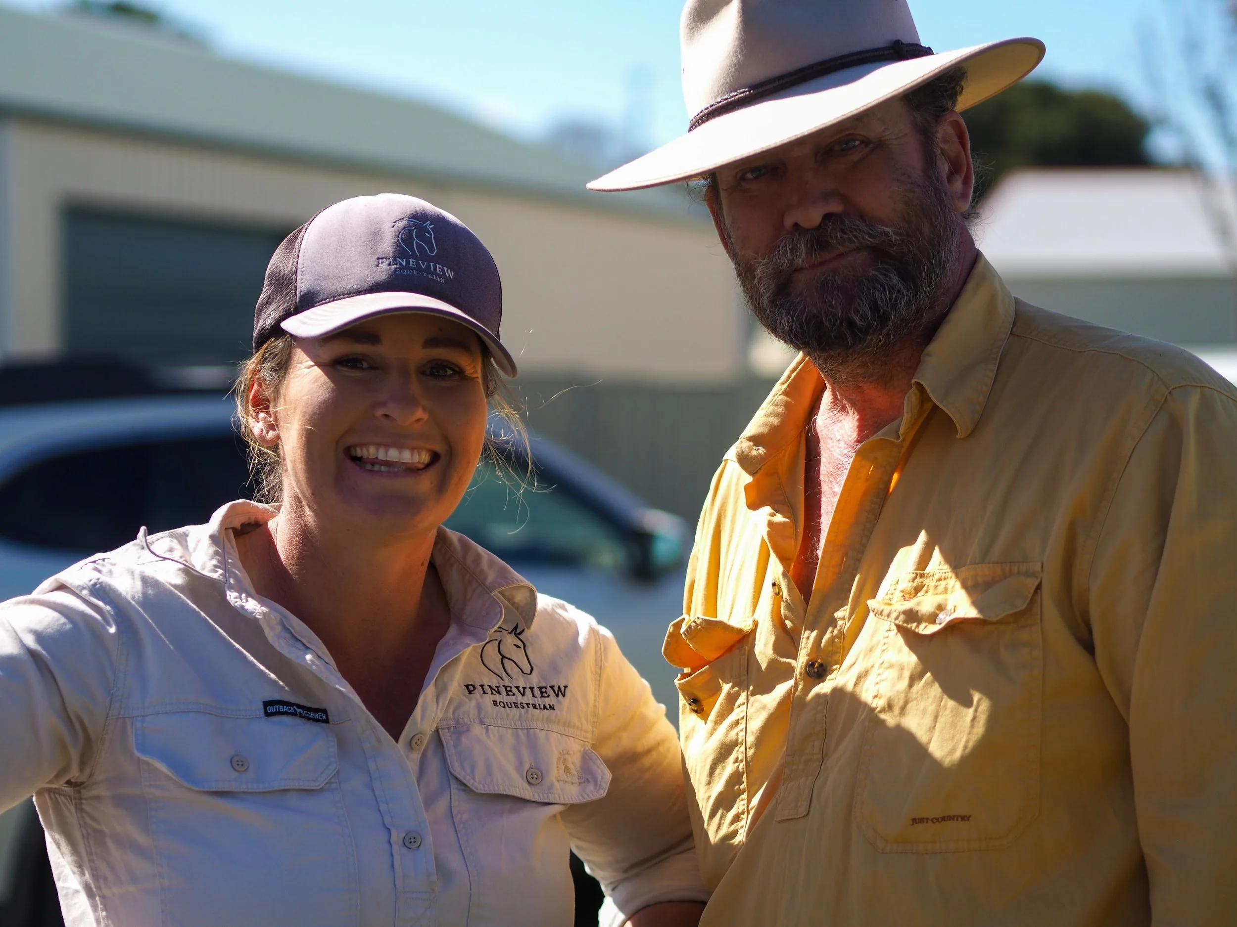 Close-up of a smiling woman wearing a beige shirt and a woman and a man in a beige shirt and a white hat at a Pineview Equestrian event outdoors.