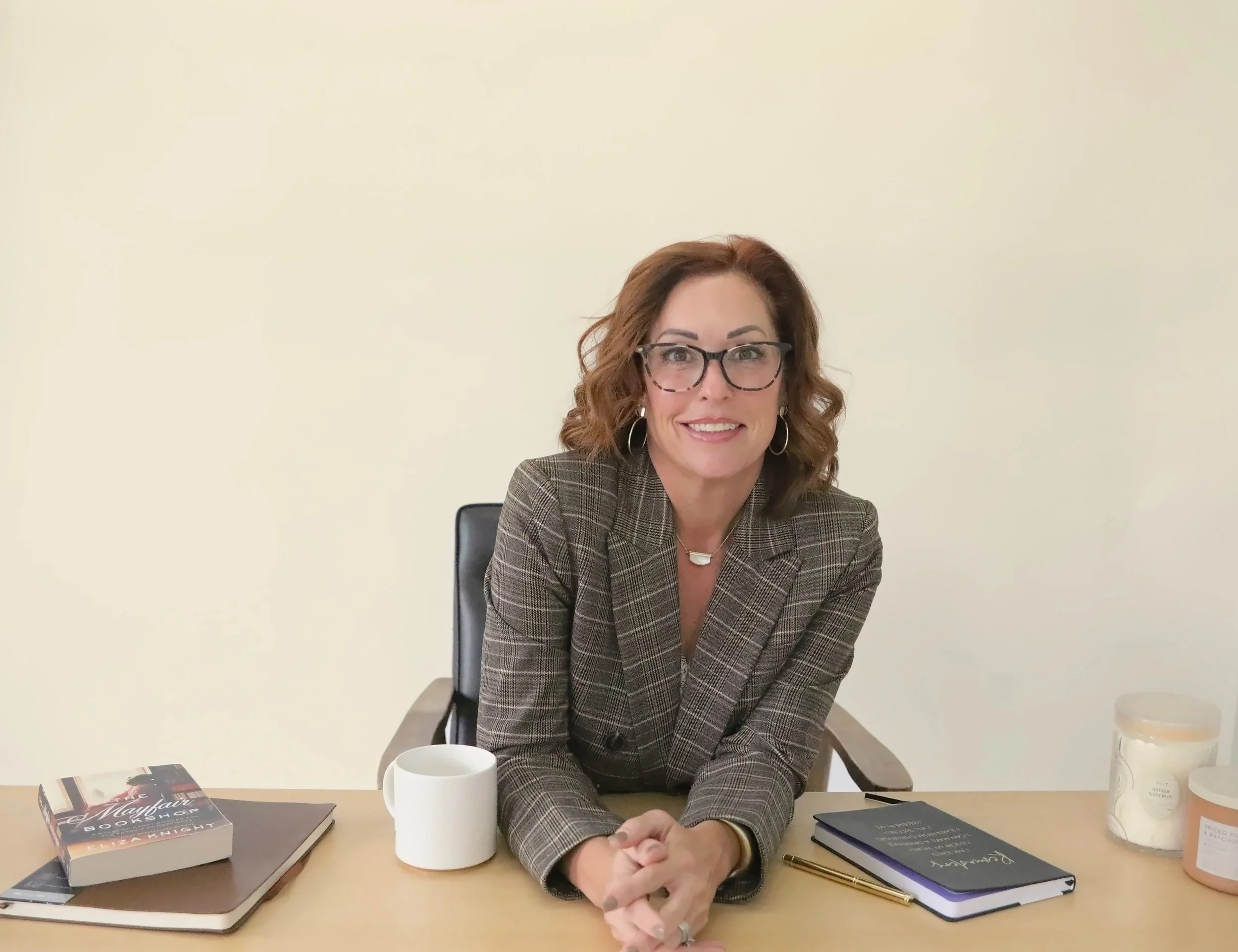 Wende Valentine at her desk in a plaid suit, hands folded