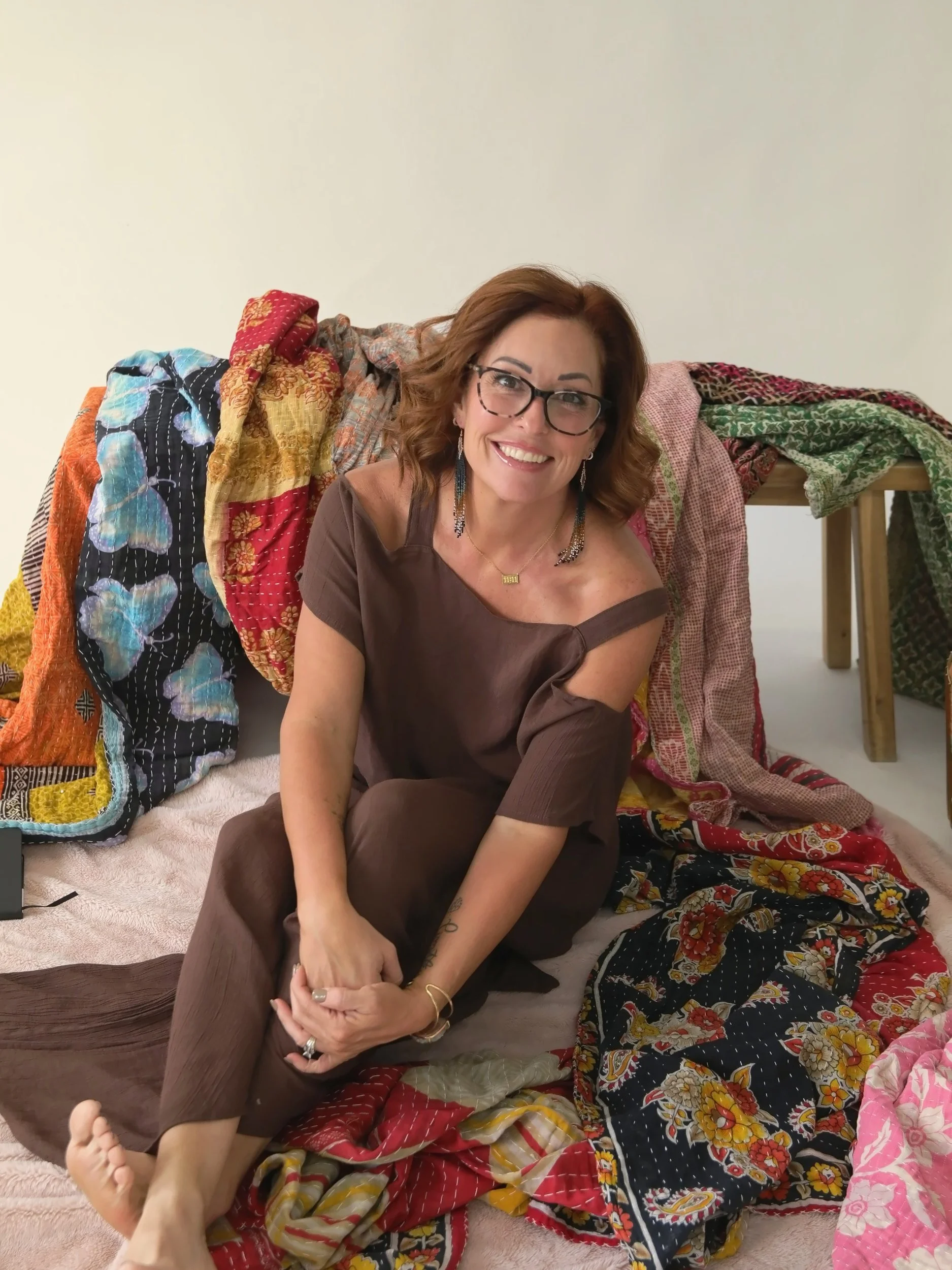 Wende Valentine smiling, seated on the floor among her colorful kantha blankets