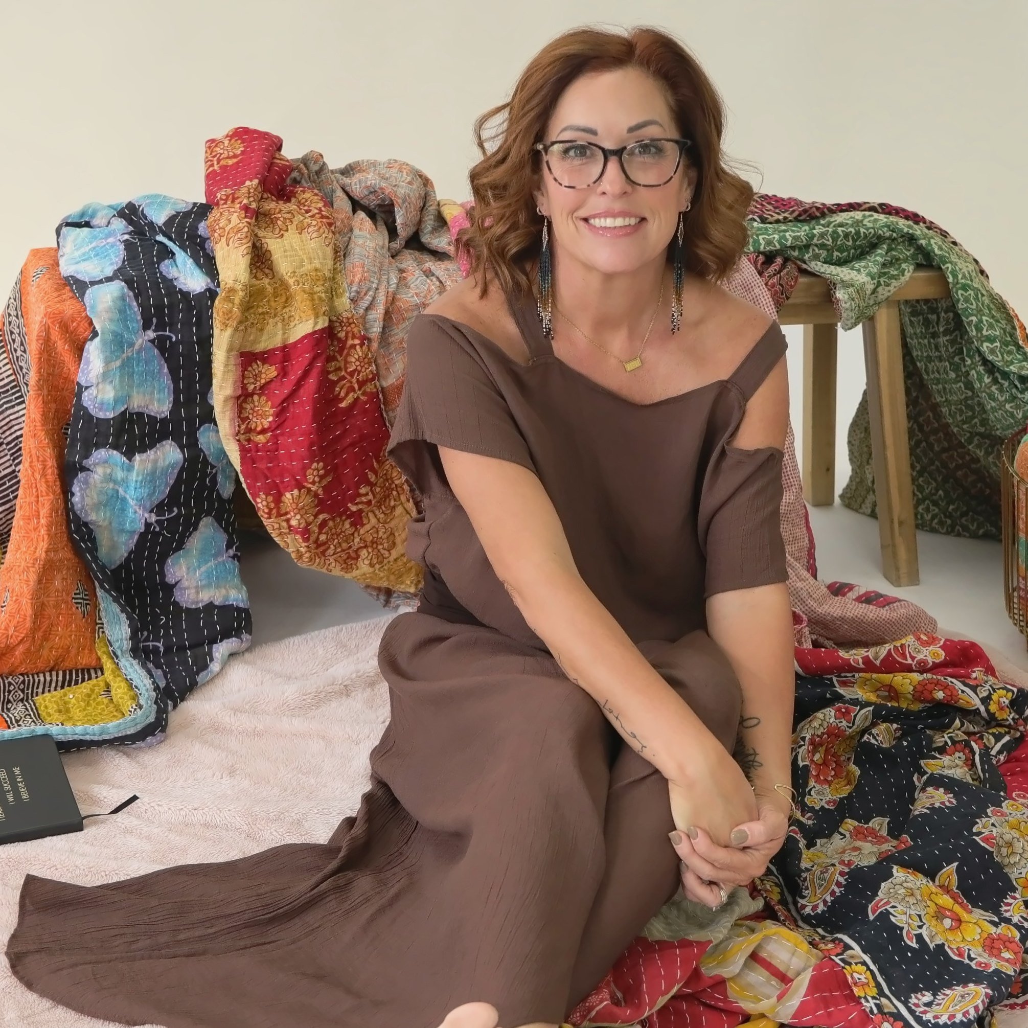 Wende Valentine smiling, seated among her colorful kantha blankets
