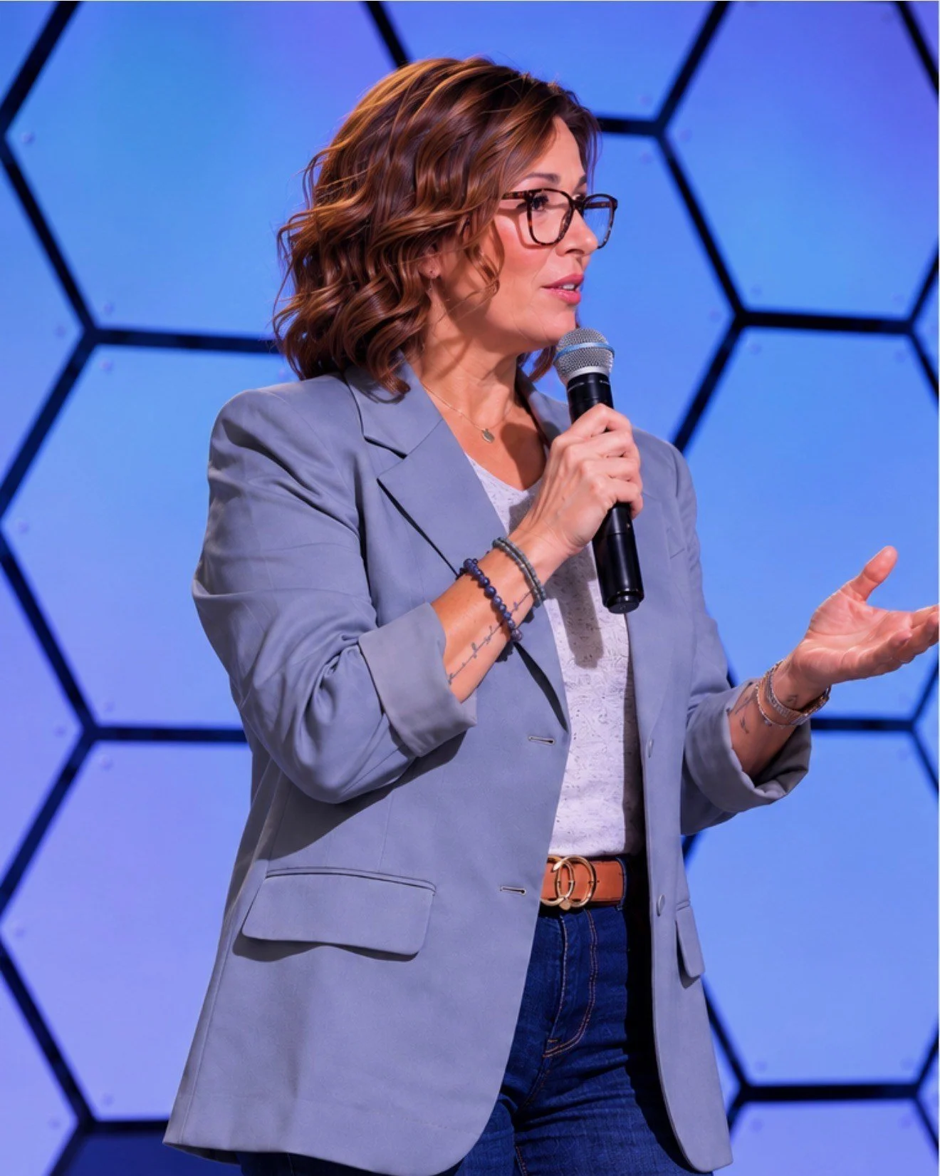 Wende Valentine speaking on stage with a microphone, hand open to the audience