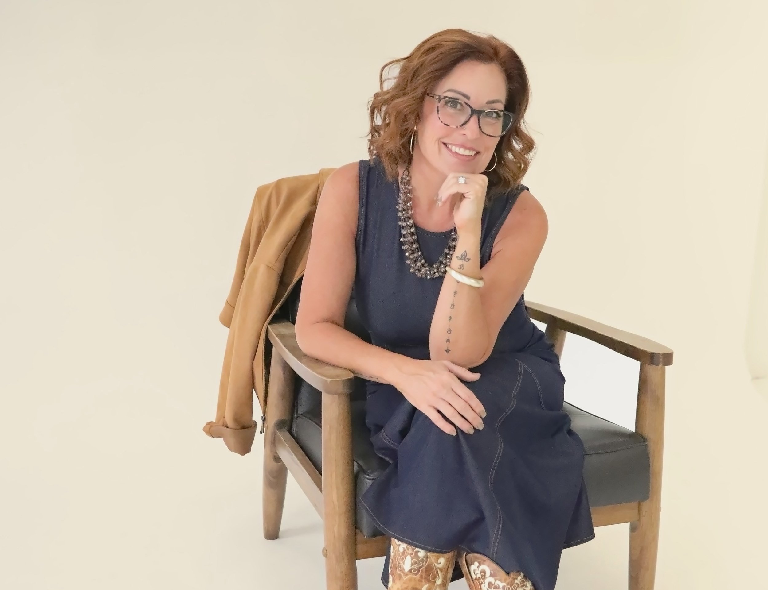 Wende Valentine in a denim dress, seated in a chair with her hand at her chin