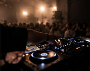 DJ mixing music at a crowded nightclub with bright lights and an enthusiastic audience.