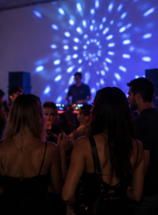 People dancing and socializing at a party with colorful disco lights on the wall.
