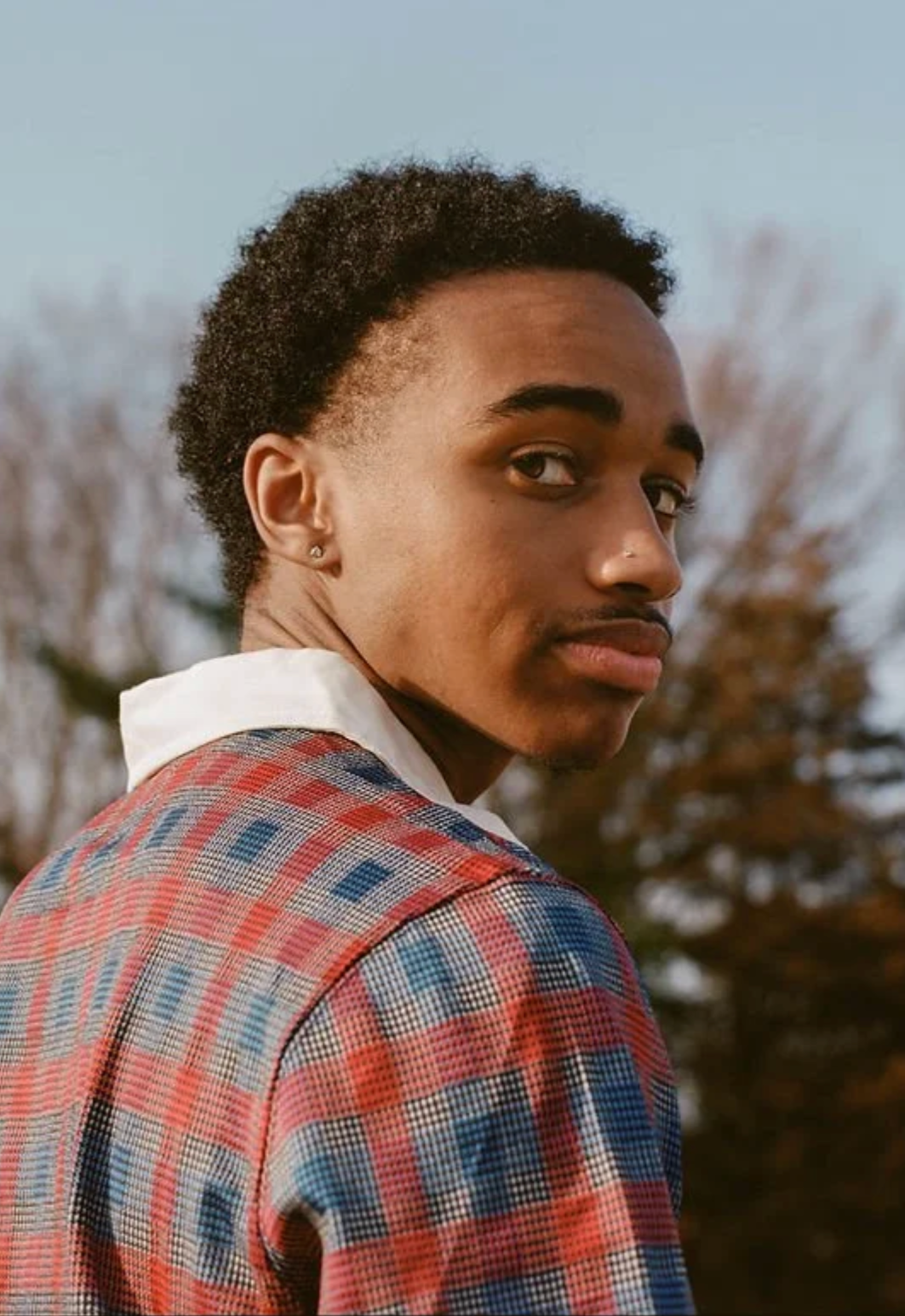 Portrait of a Rosiah with short curly hair wearing a red and blue plaid shirt outdoors