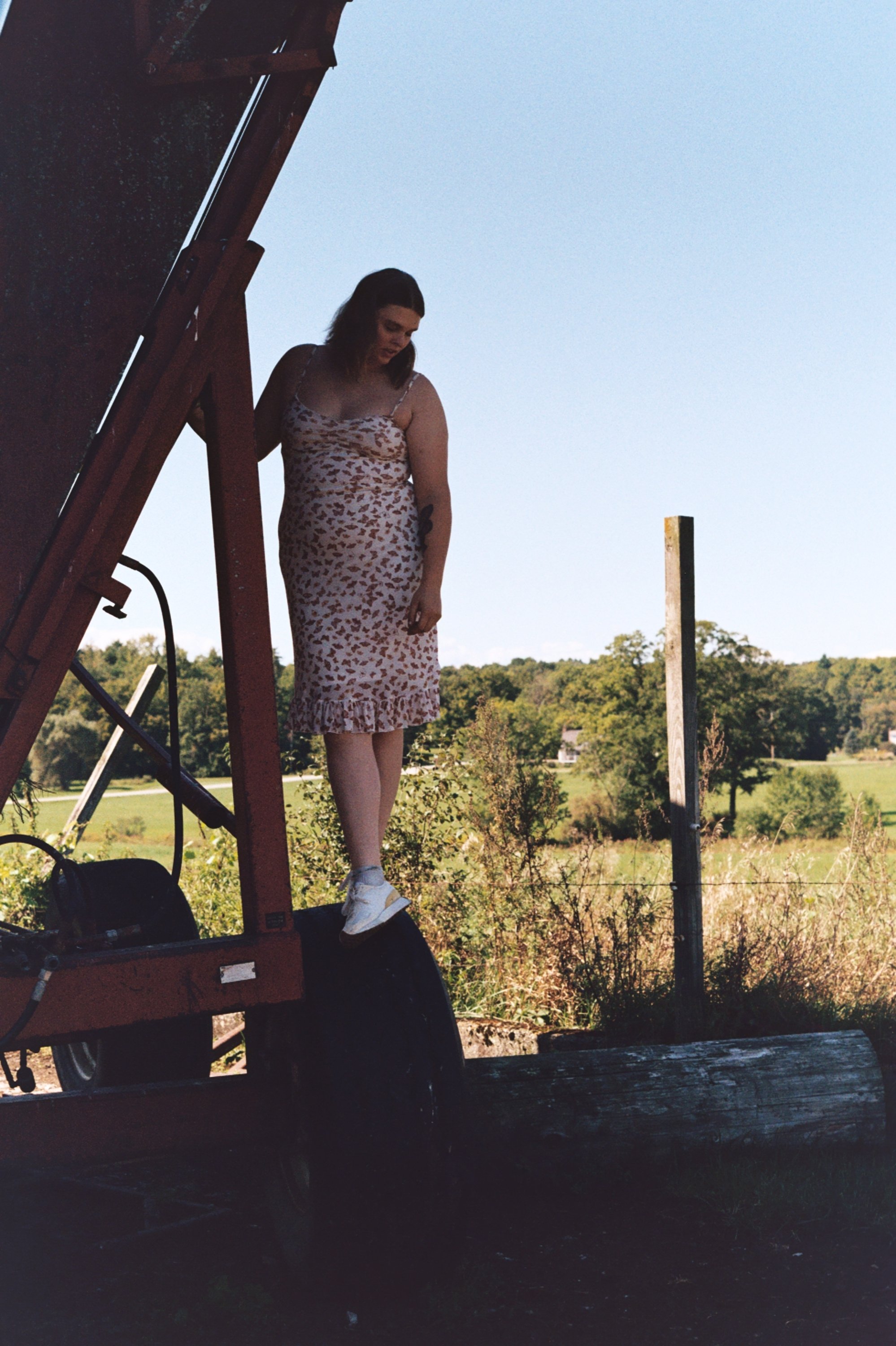 A woman in a sleeveless dress with a leopard print pattern is standing on a lift platform outdoors, with a scenic landscape of trees and a clear sky in the background.
