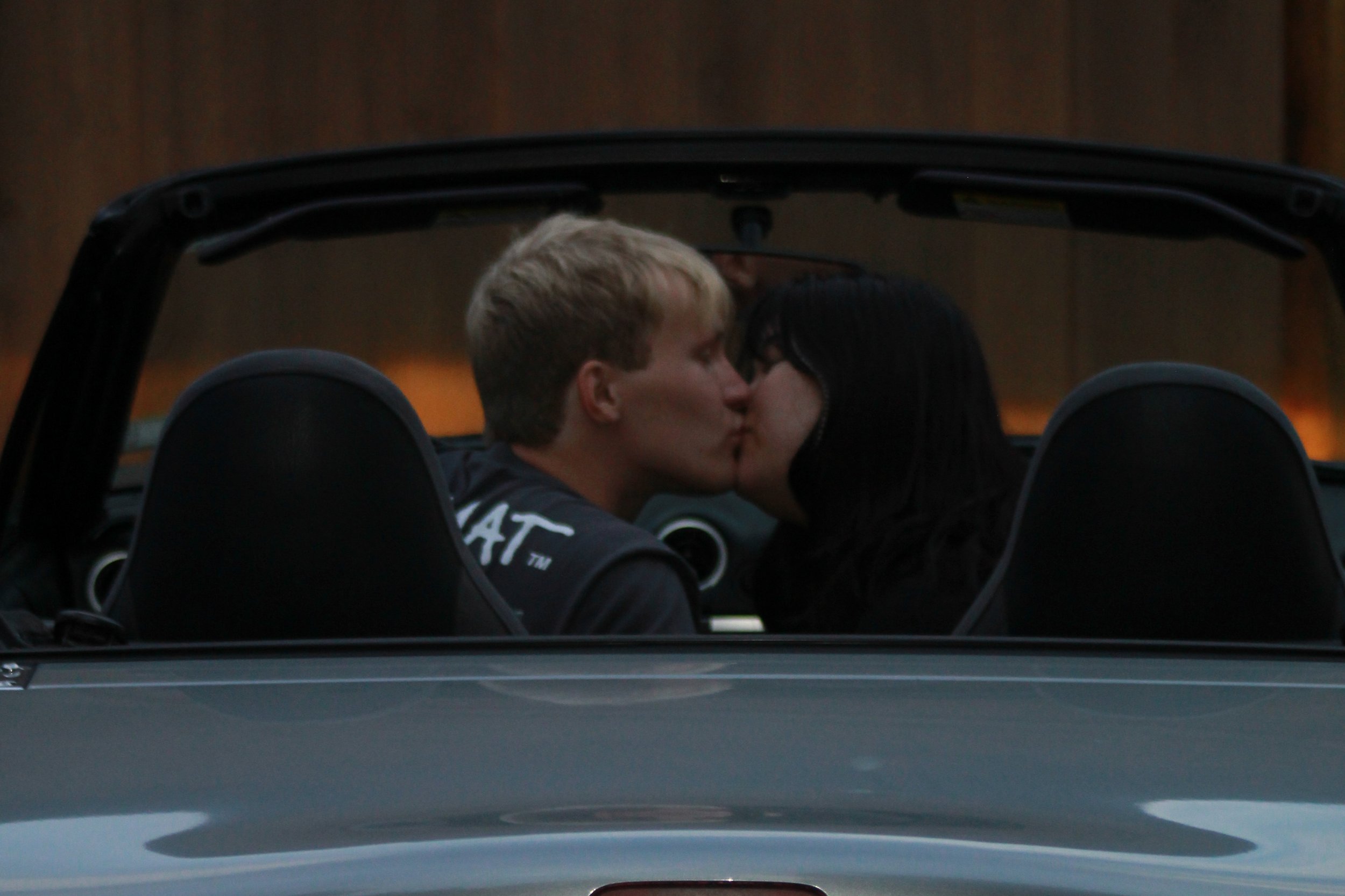 A couple sharing a kiss inside a convertible car with the roof down during sunset.