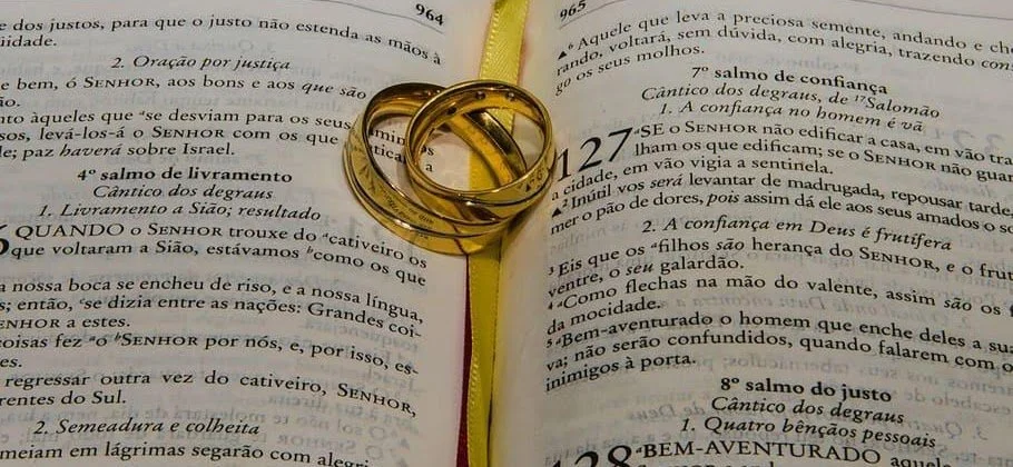Two gold wedding rings stacked on an open Bible with yellow ribbon marker.