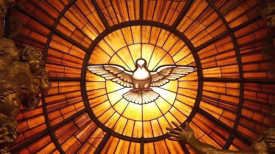A stained glass ceiling featuring a dove with outspread wings, illuminated from behind, with ornate golden sculptures on the sides.