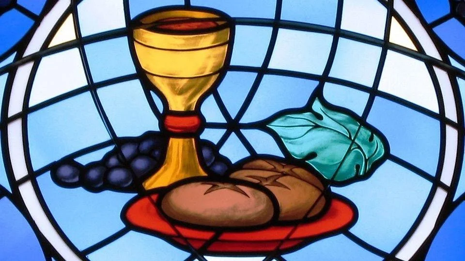 A stained glass design featuring a chalice, grapes, bread, and a leaf.