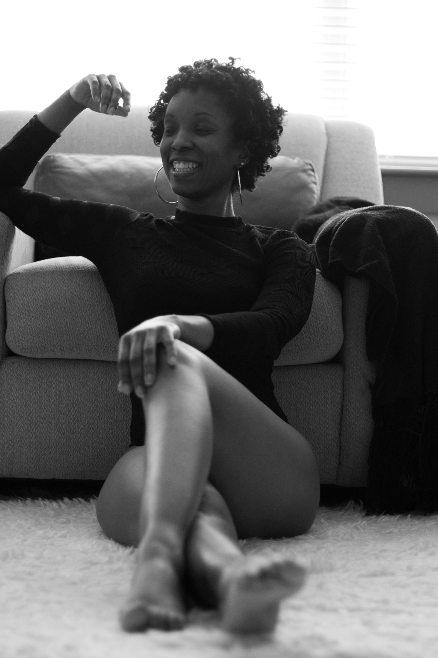 A smile breaks the stillness. Seated against the chair with one hand lifted, she brings a spontaneous warmth to the quieter portraits around her.