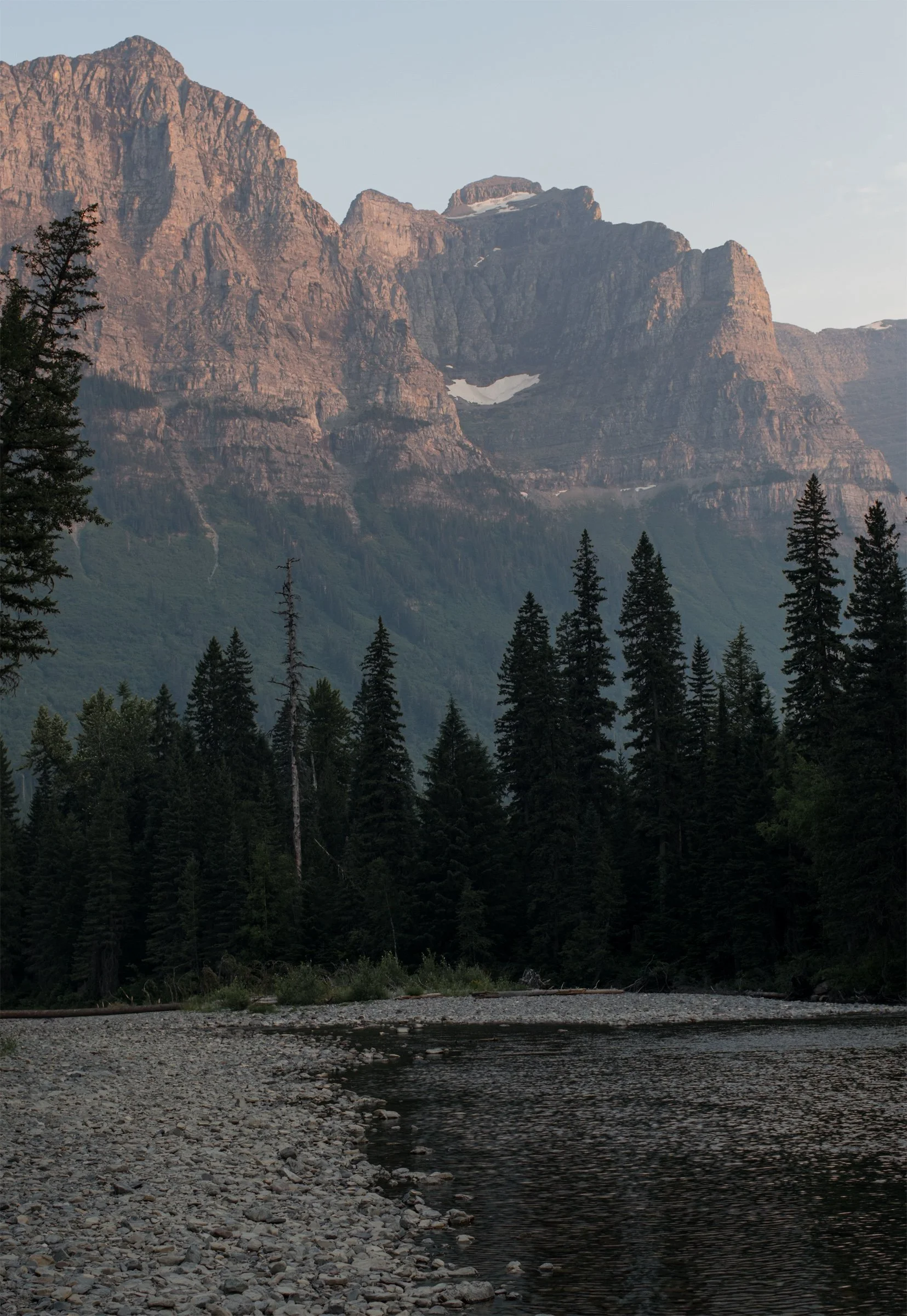 Warm light touches a rocky mountain above a cool lake and dark shoreline trees. The day gathers into stillness.
