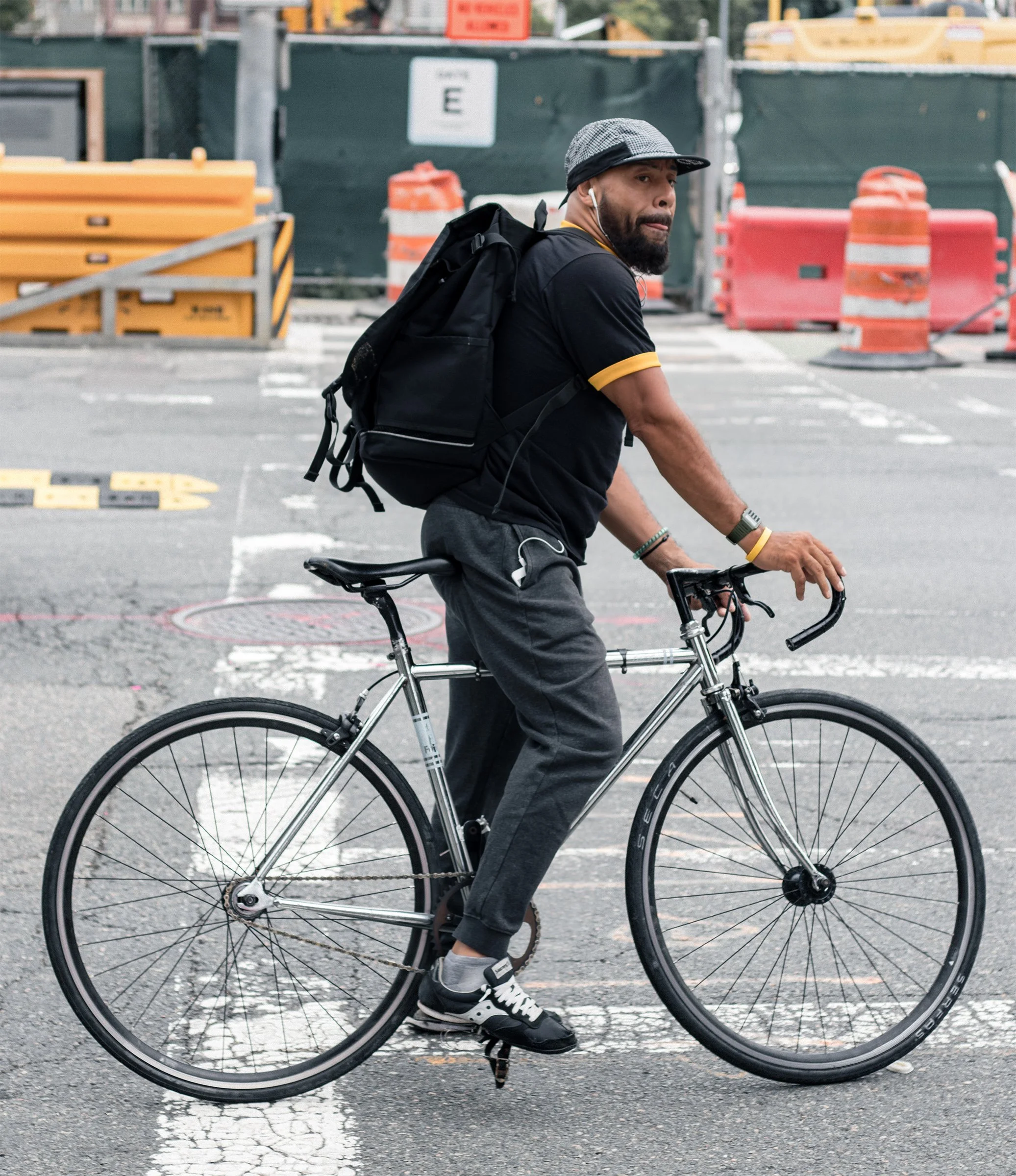 A cyclist turns toward the camera as he rides past construction barriers.