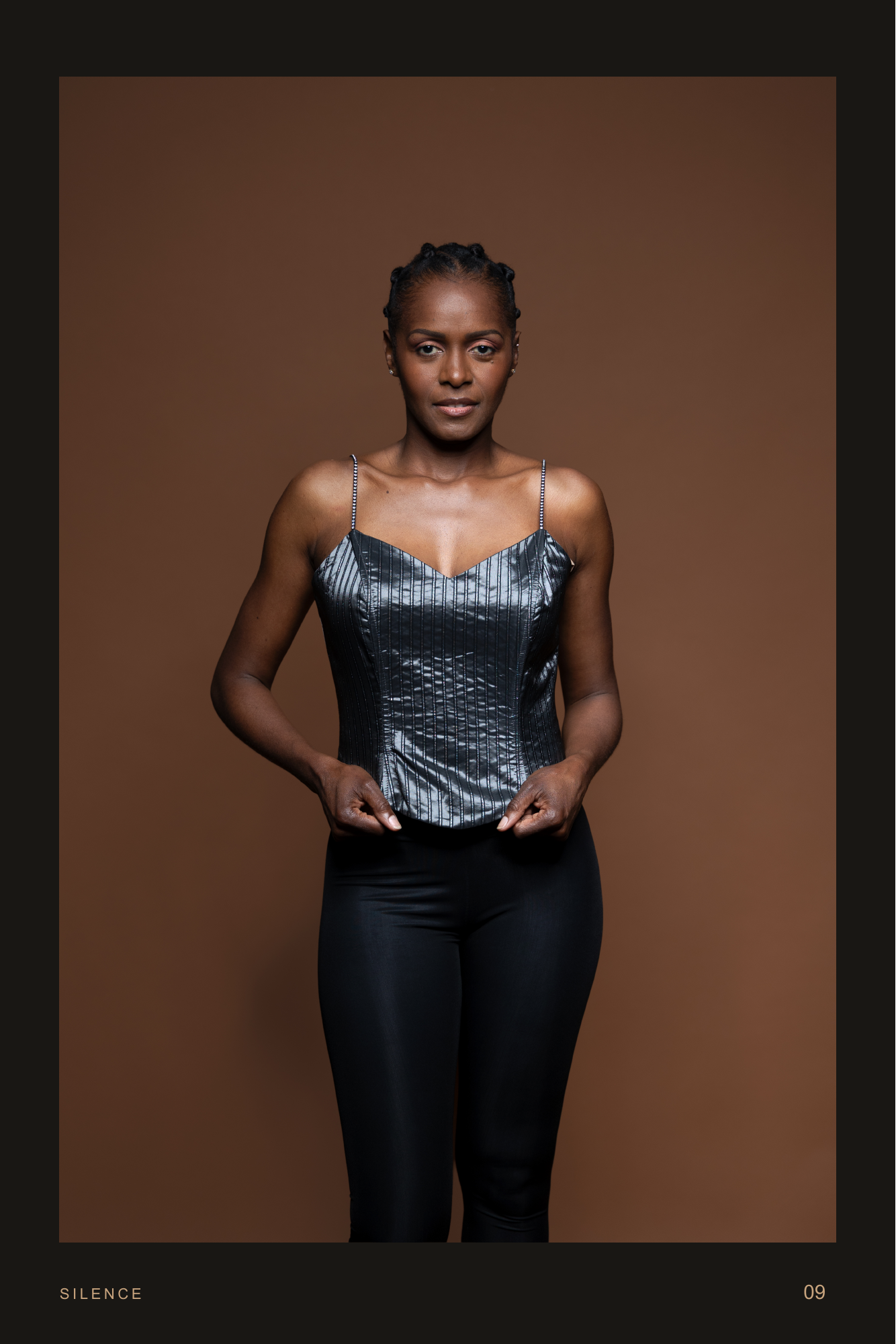 Strength In Grace, page 9. She faces the camera directly, lightly holding the corset’s hem.