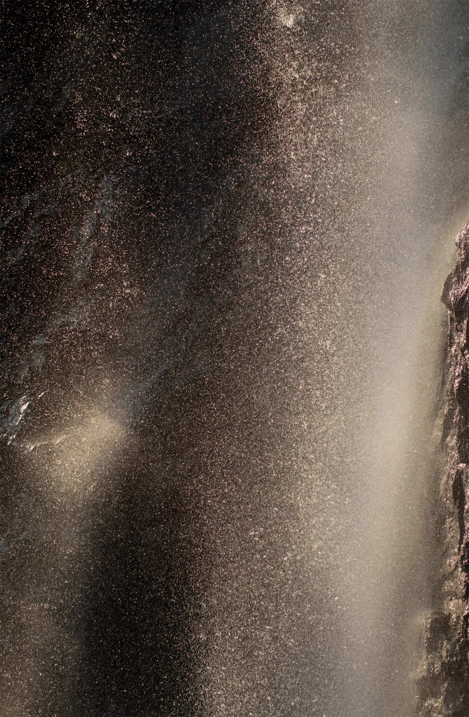 White water and drifting spray dissolve into luminous movement beside a dark rock edge. For a moment, movement has no edges.