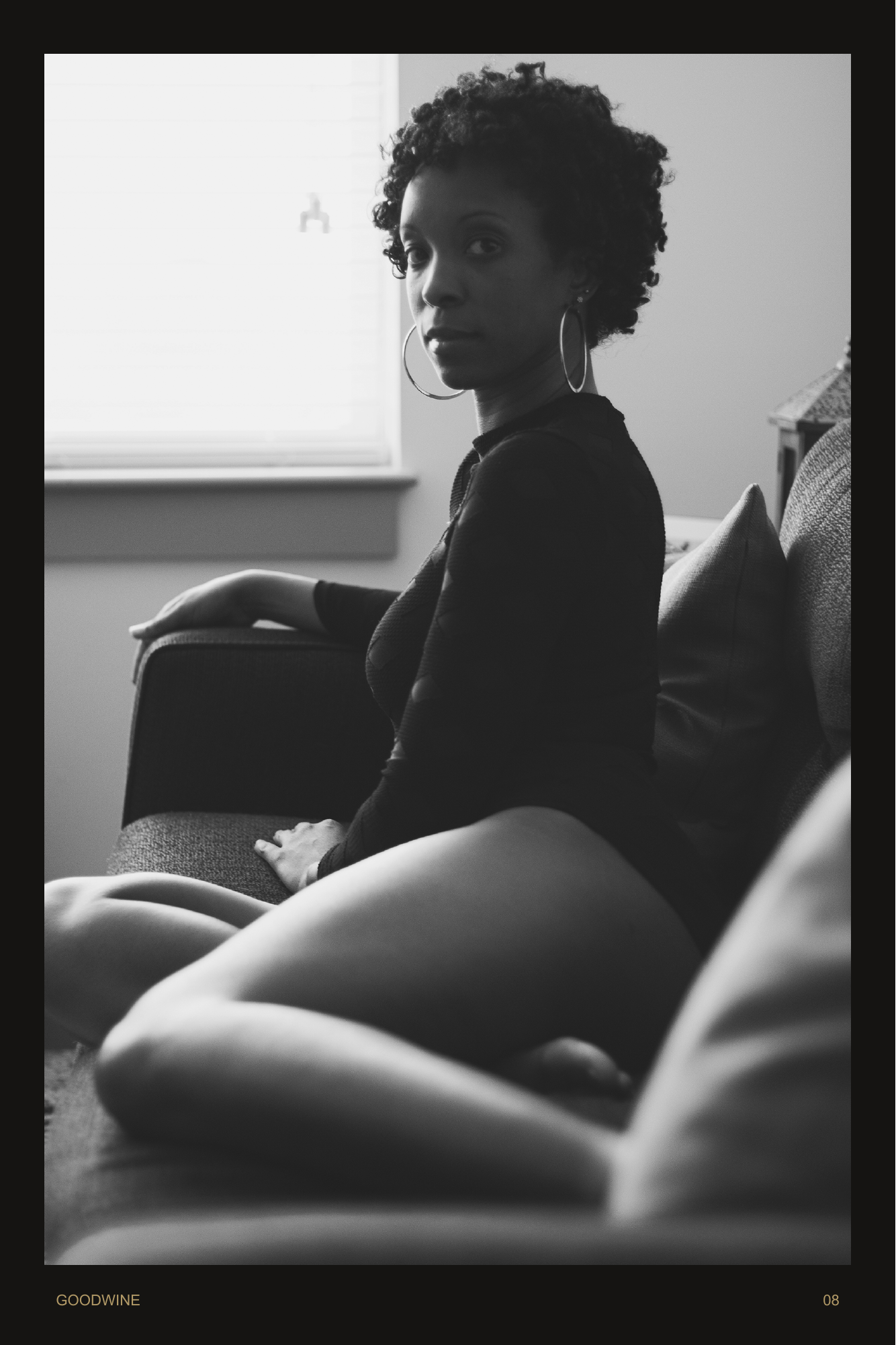 Page 8. Seated beside the window, she turns back toward the camera. A monochrome portrait with an intimate, unhurried gaze.