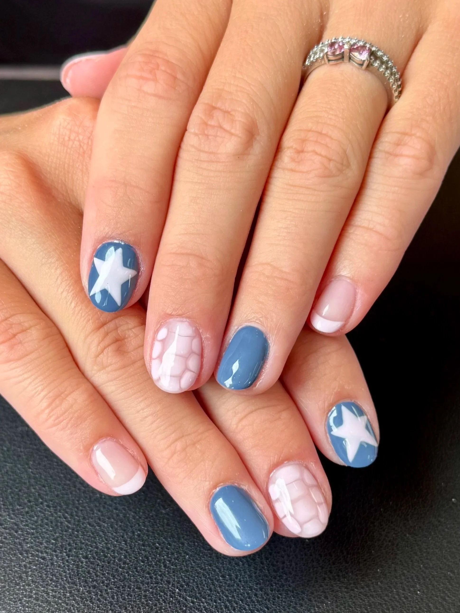 Close-up of a hand with beautifully decorated nails, some with stars and shells, and a silver ring with pink gemstones.