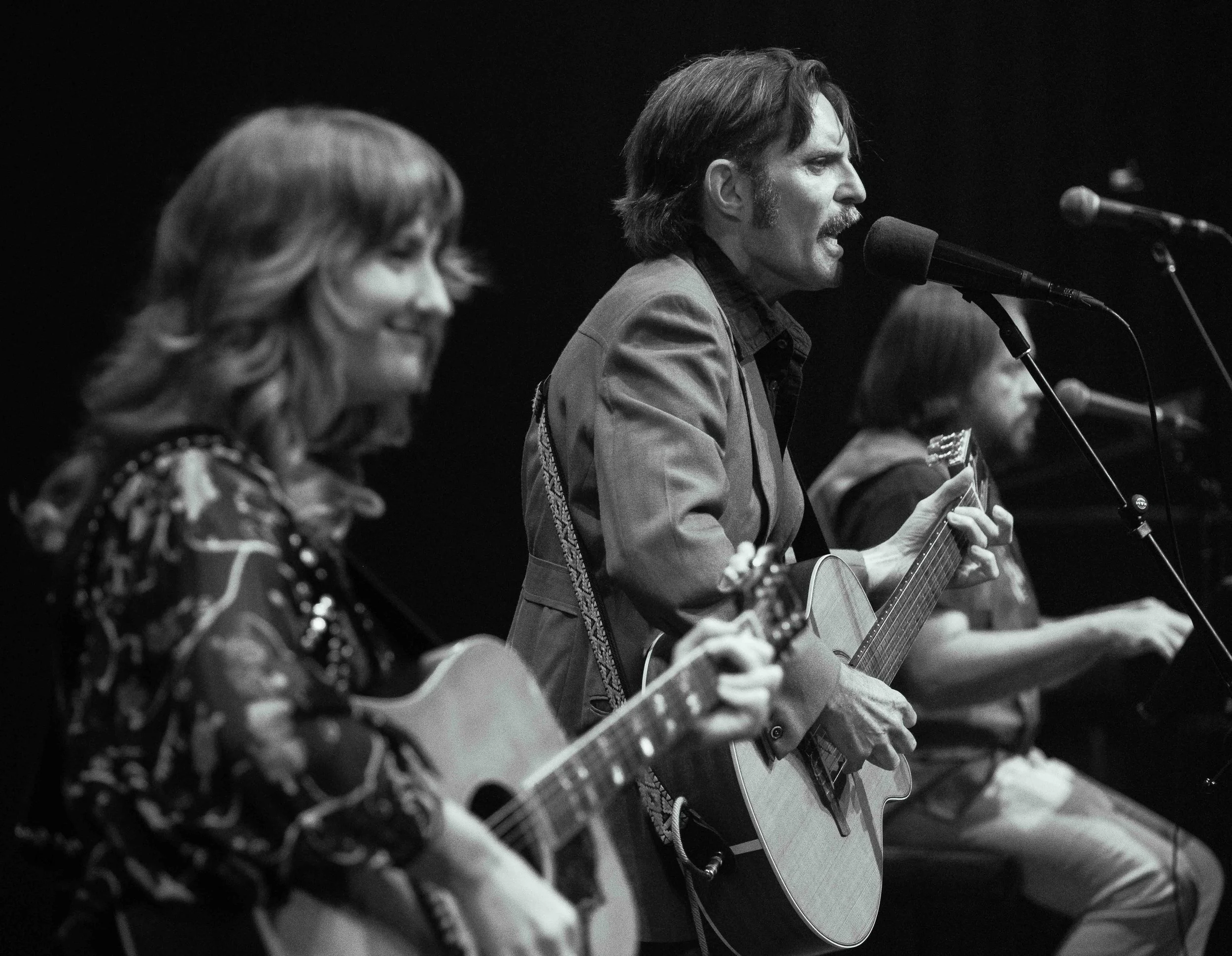 Three musicians playing guitars and singing into microphones during a performance.