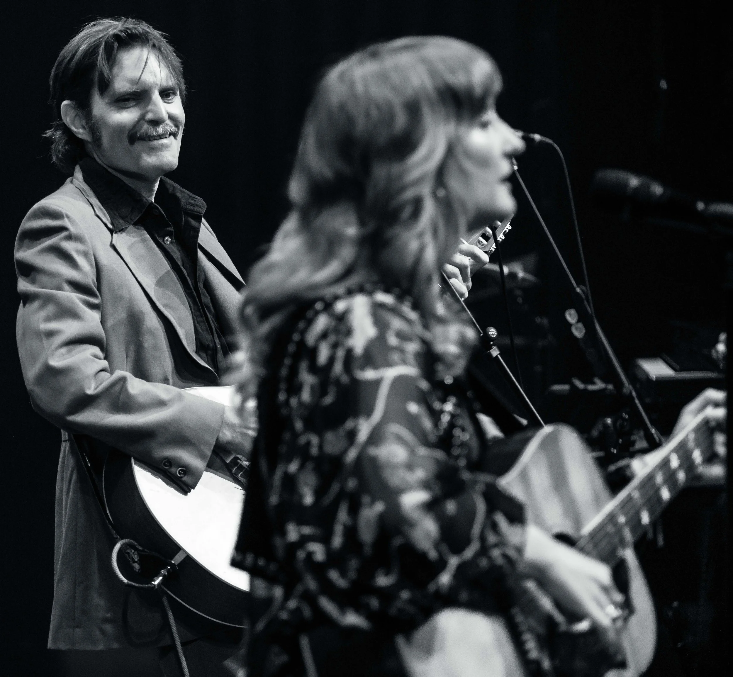 Black and white photograph of a man smiling while seated at a piano, with a woman singing into a microphone in front of him.