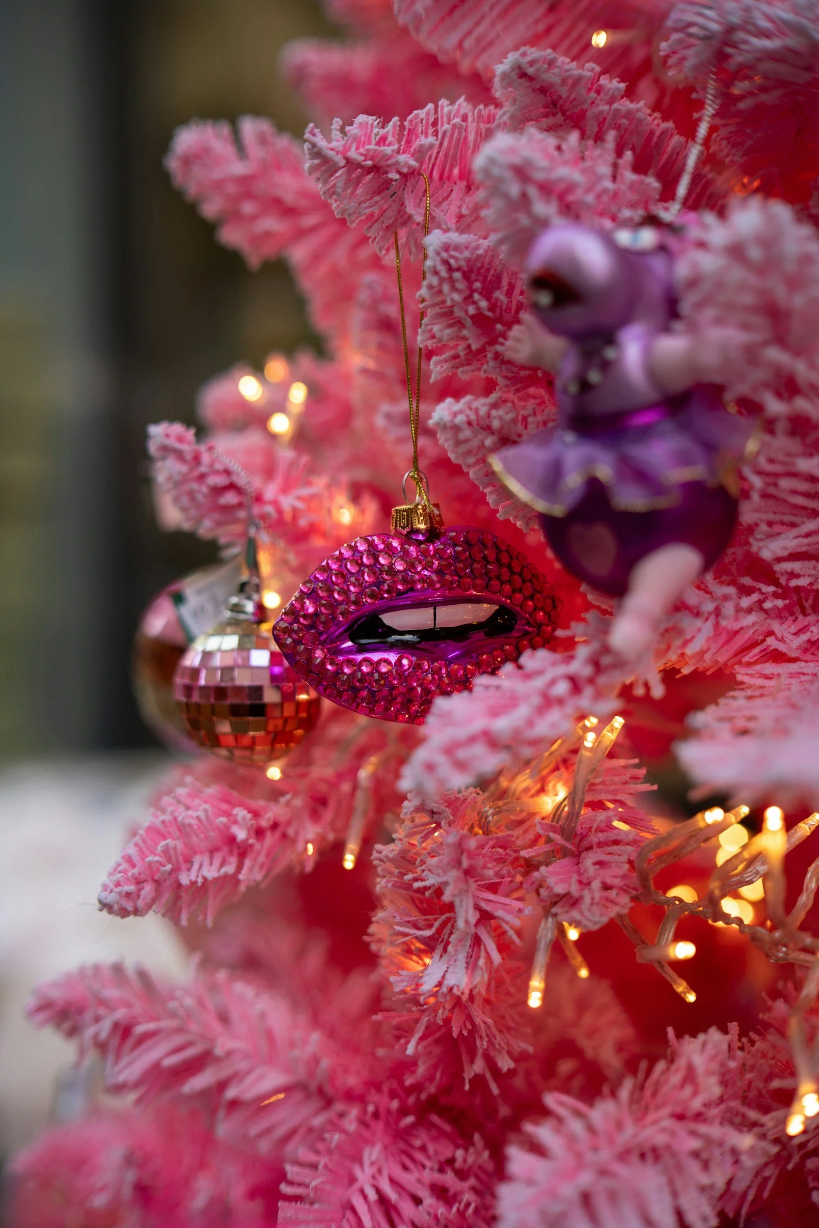 Close-up of pink artificial Christmas tree with pink ornaments and warm lights