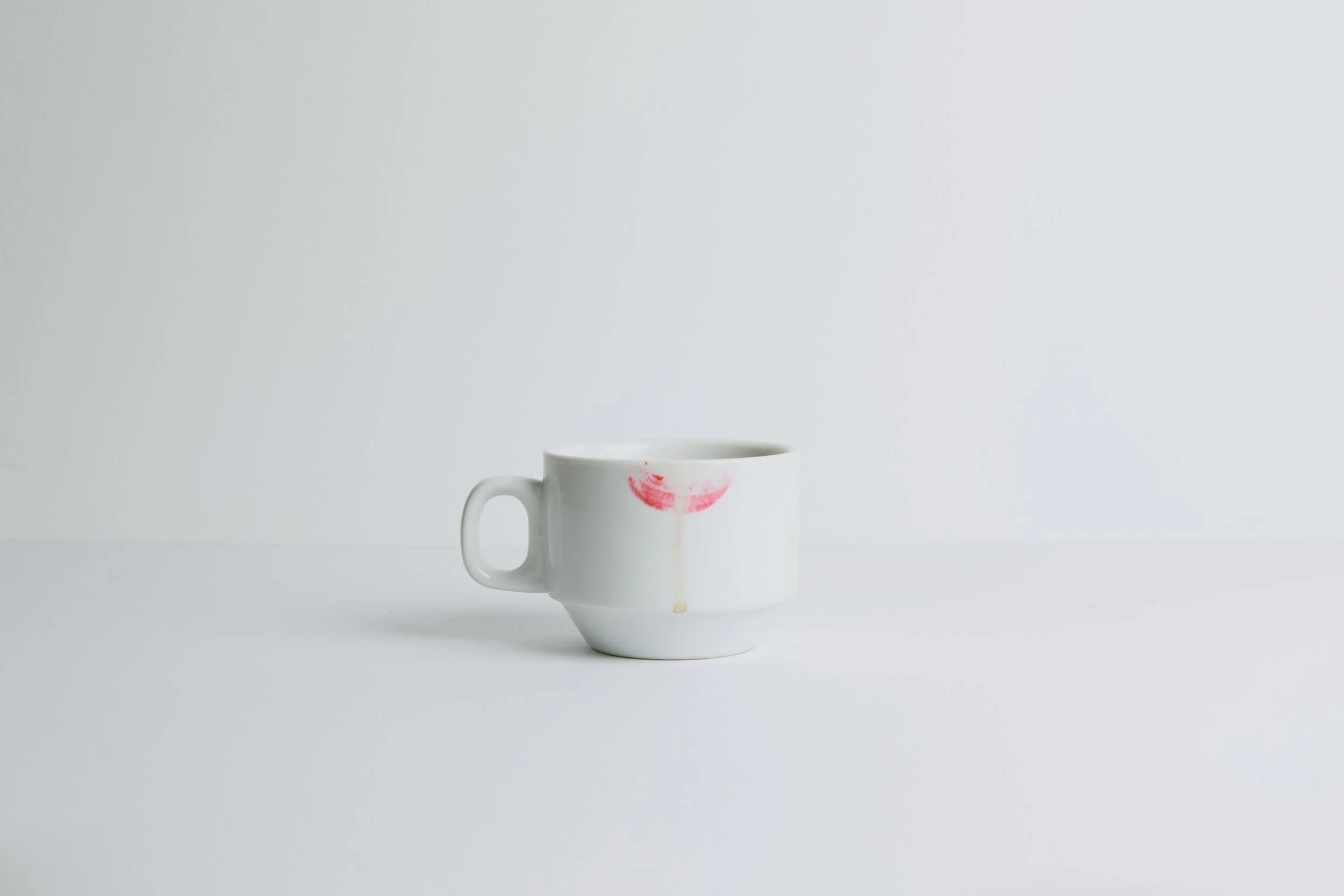 White coffee mug with a lipstick mark stain on it, placed against a plain light gray background.