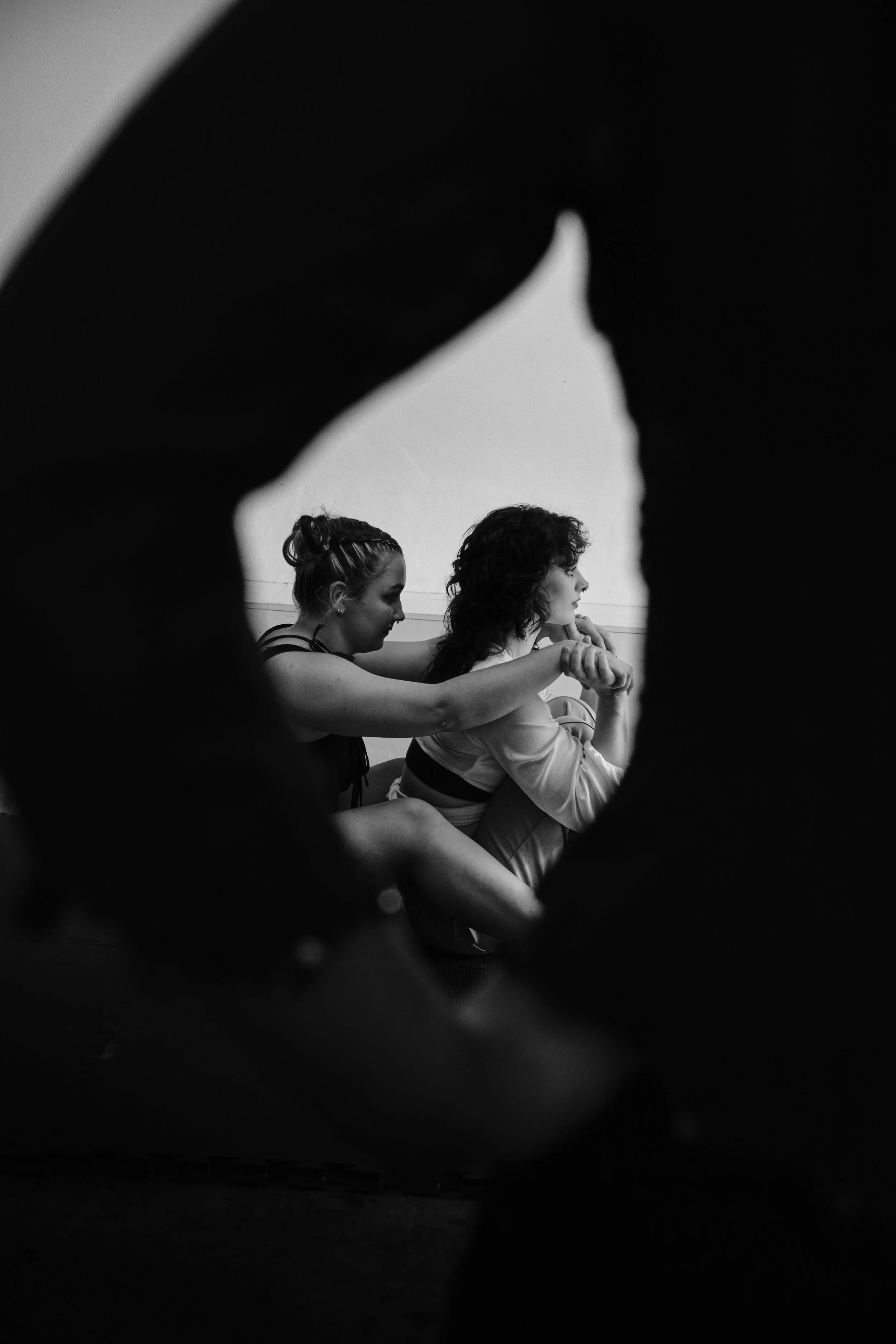 Two women sitting close together, practicing yoga or meditation, viewed through a circular opening, in black and white, circus artist collaboration.