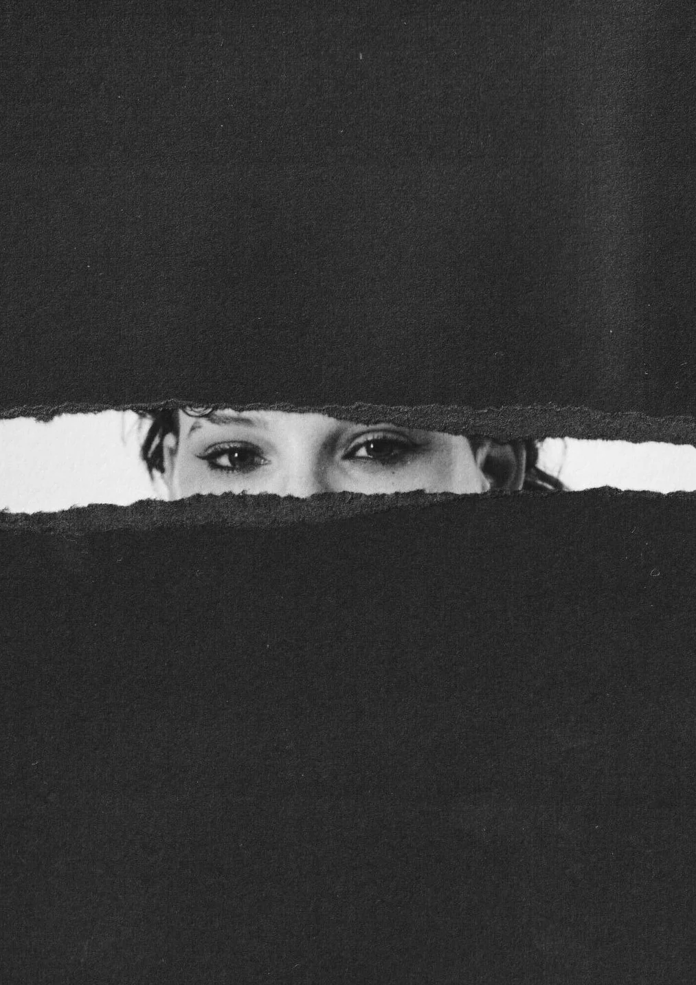 A woman peeking through a torn gap in black paper, with only her eyes and part of her face visible, collage circus arts photography.
