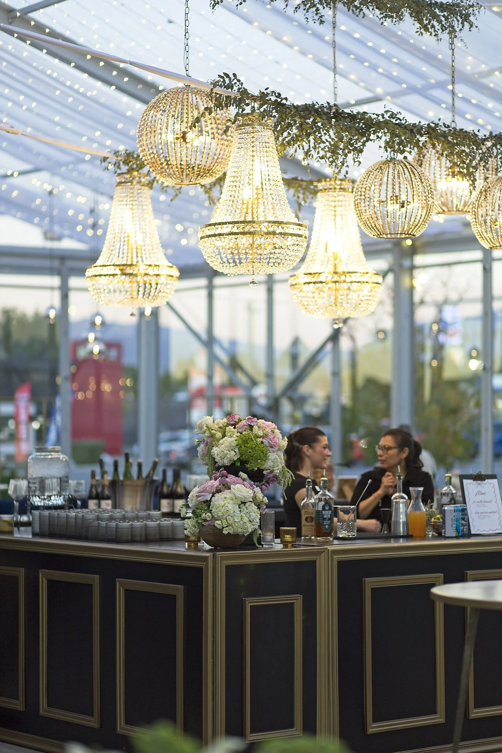 Chandeliers hanging from a ceiling above a floral centerpiece at an elegant indoor event or reception.