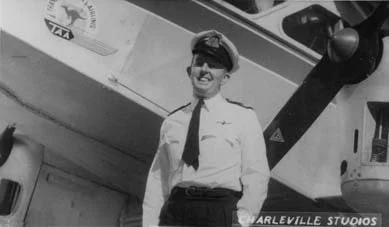 Black and white photo of a woman in a pilot's uniform smiling in front of an airplane at Harleville Studios.