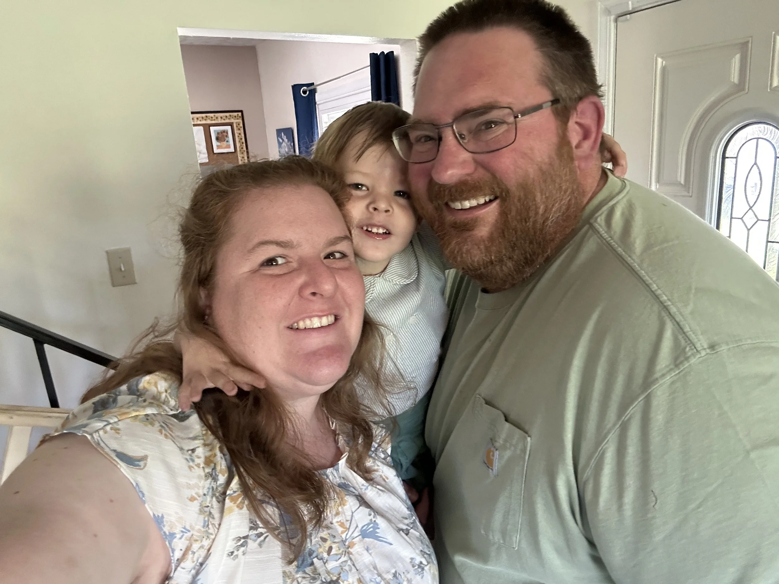 A family of four smiling and hugging in a house, with a woman, a man with glasses, and two children.